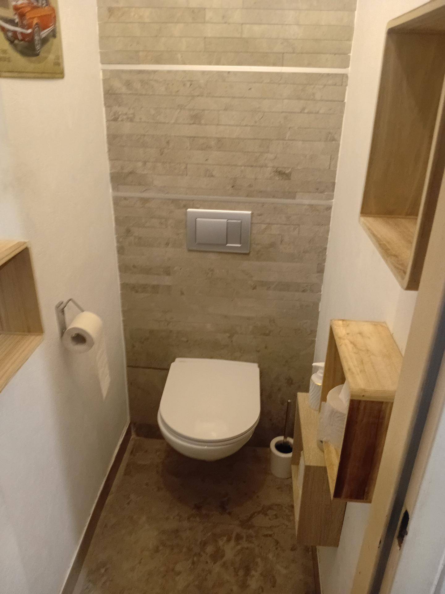 Modernes Gäste-WC mit wandhängender Toilette, Steinoptikfliesen und Holzregalen.