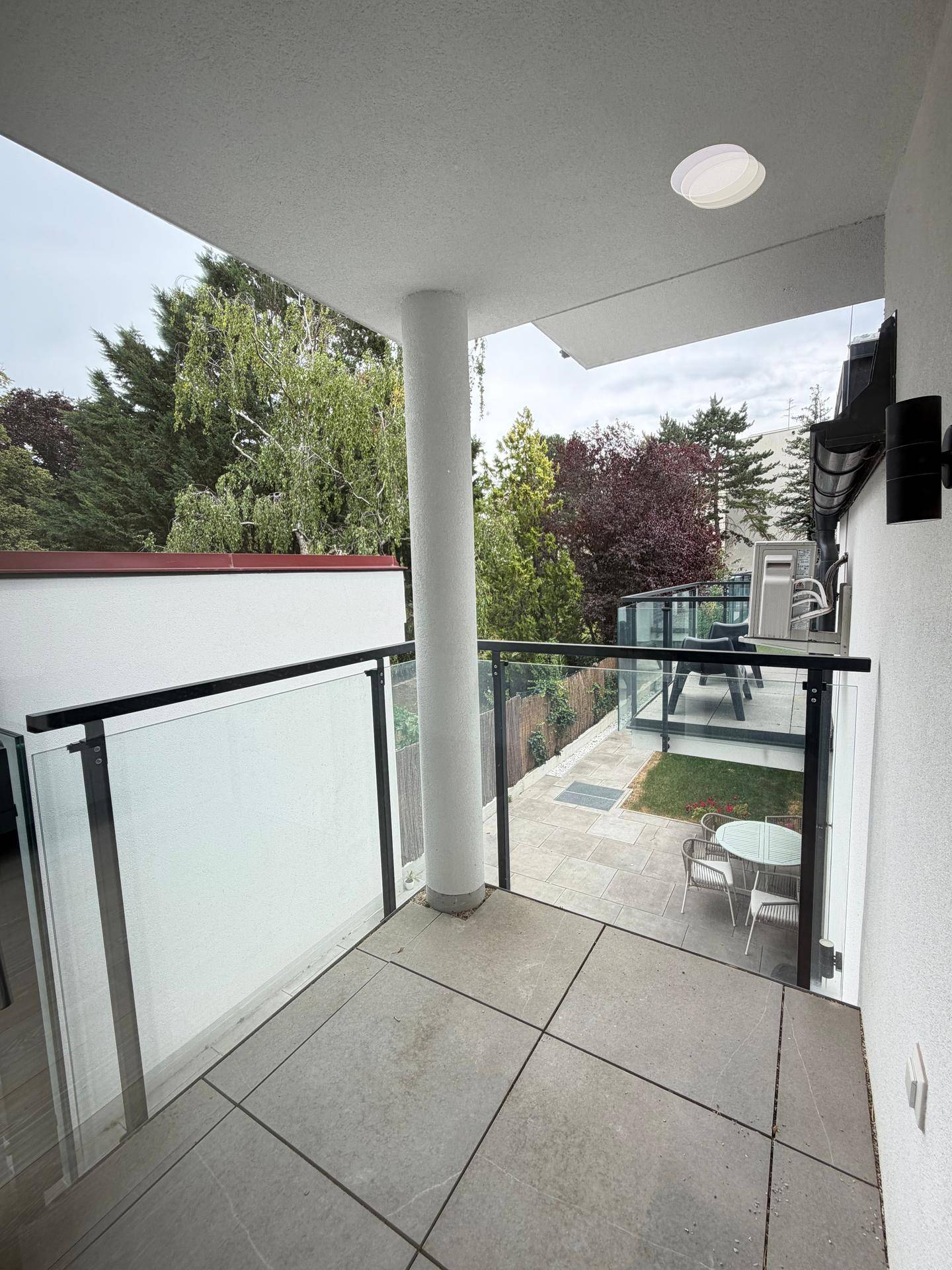 Moderner Balkon mit Glasgeländer, Fliesenboden und Blick ins Grüne.