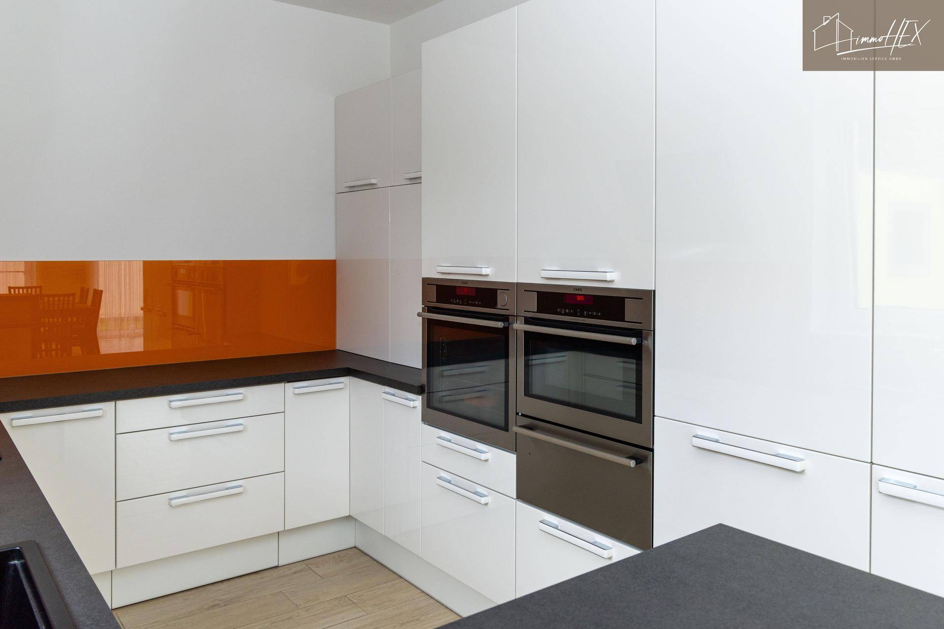Elegante weiße Küche mit zwei integrierten Öfen und orangefarbener Rückwand.