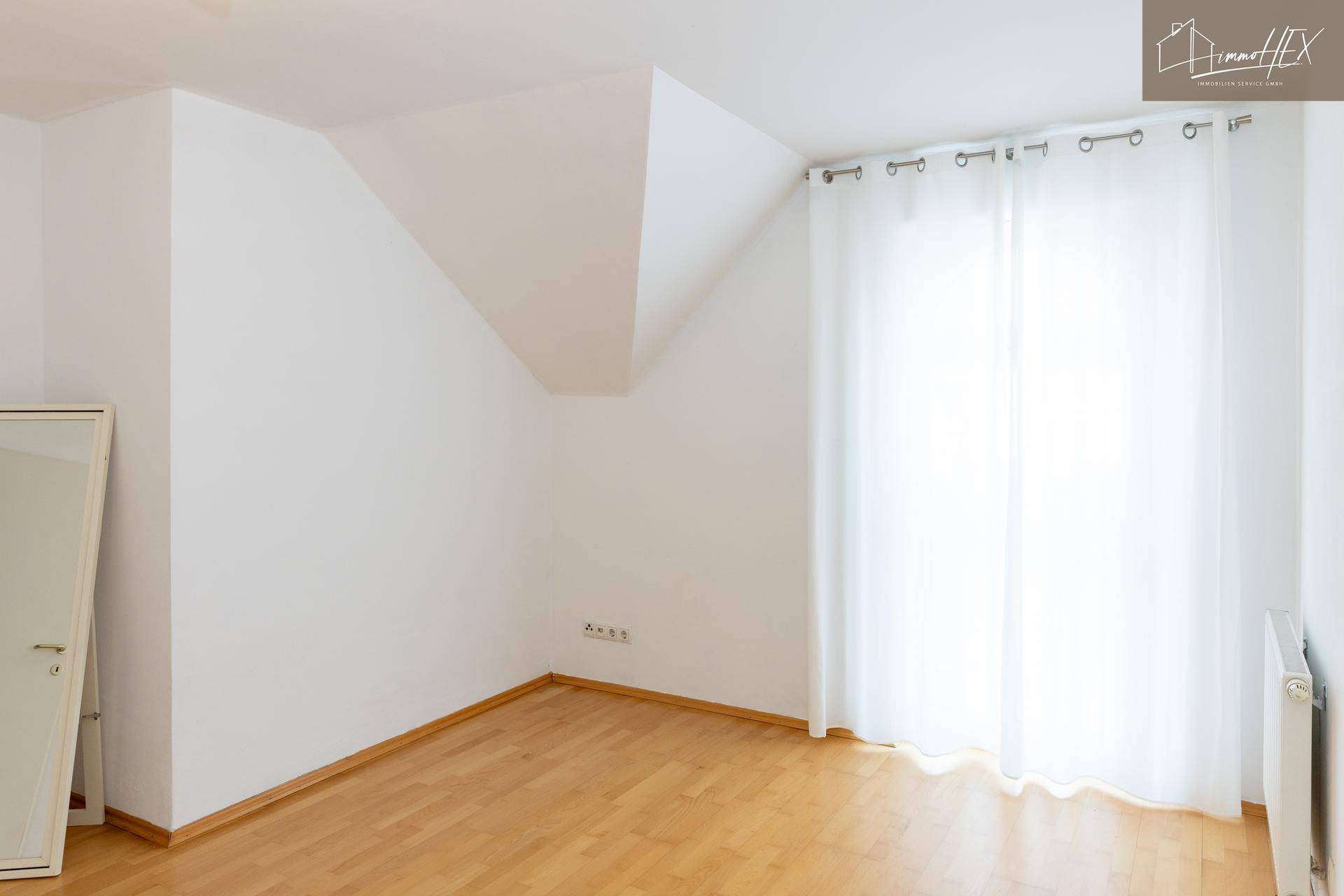 Leeres Zimmer im Dachgeschoss mit Holzboden, weiß gestrichenen Wänden und Dachschräge.