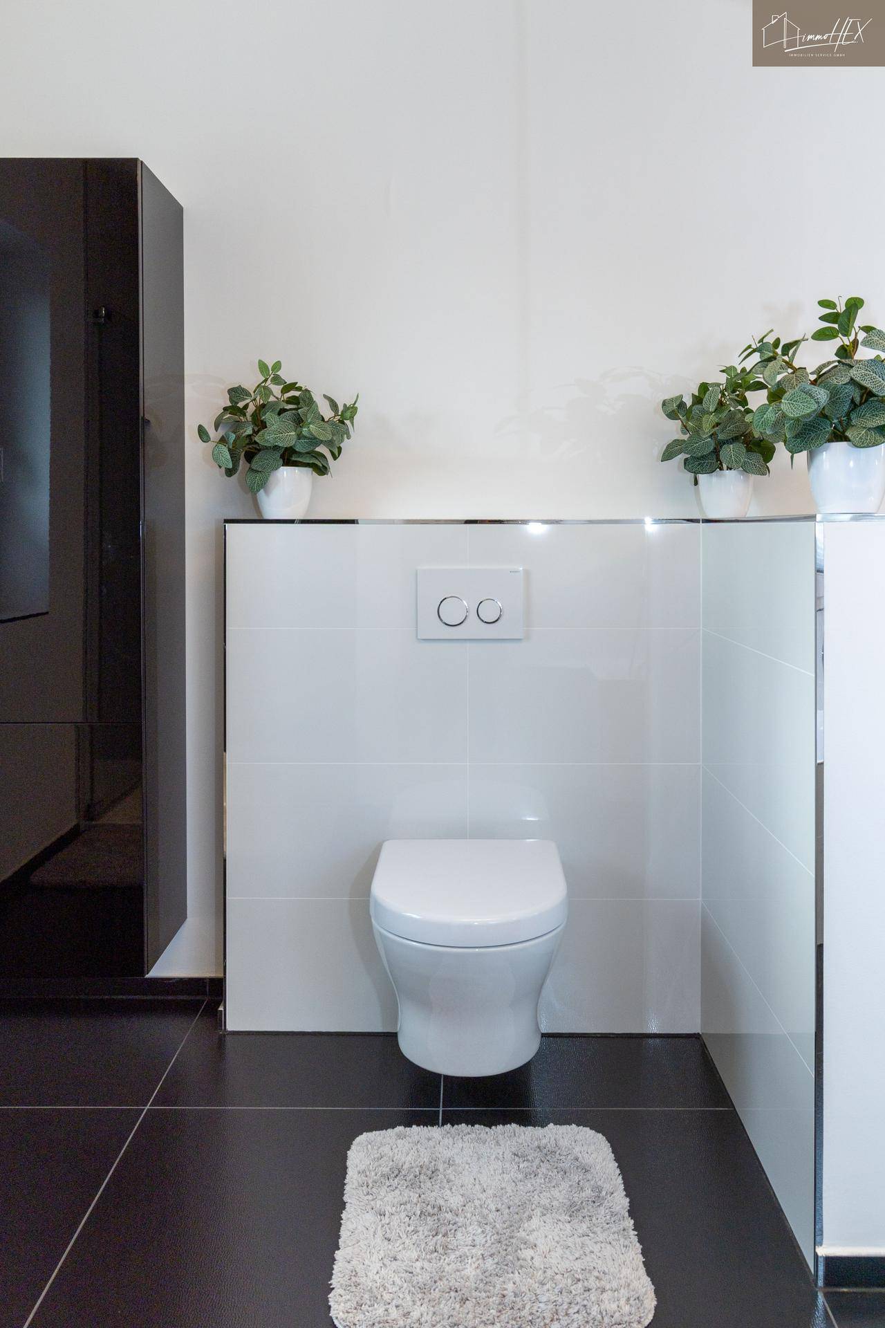 Wandhängende Toilette mit Spülkasten und Pflanzen in einem modernen Badezimmer.