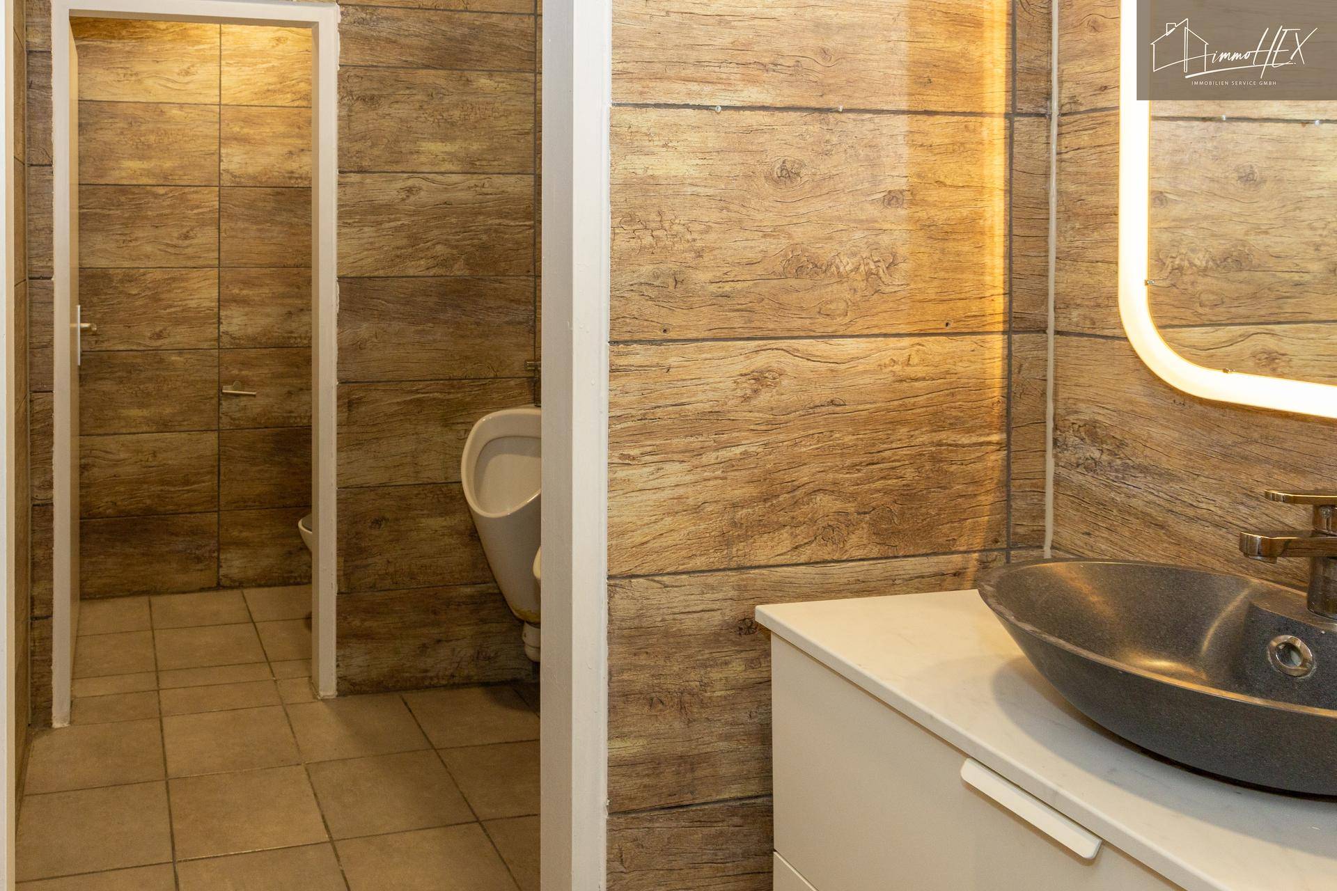 Toilettenbereich mit Urinal, modernem Waschbecken und holzgemusterten Fliesen.