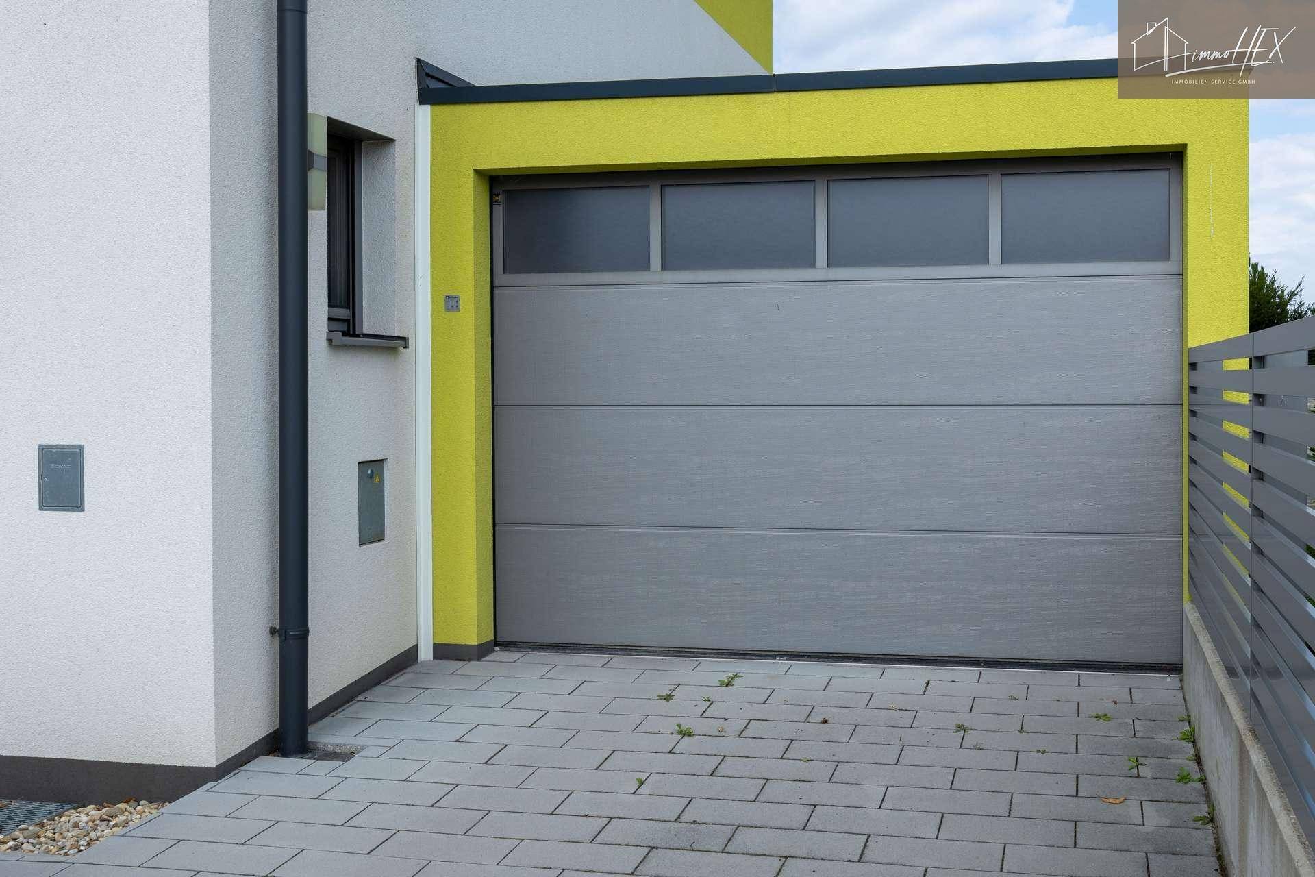 Moderne Garage mit grauem Rolltor und gepflasterter Zufahrt neben dem Haus.
