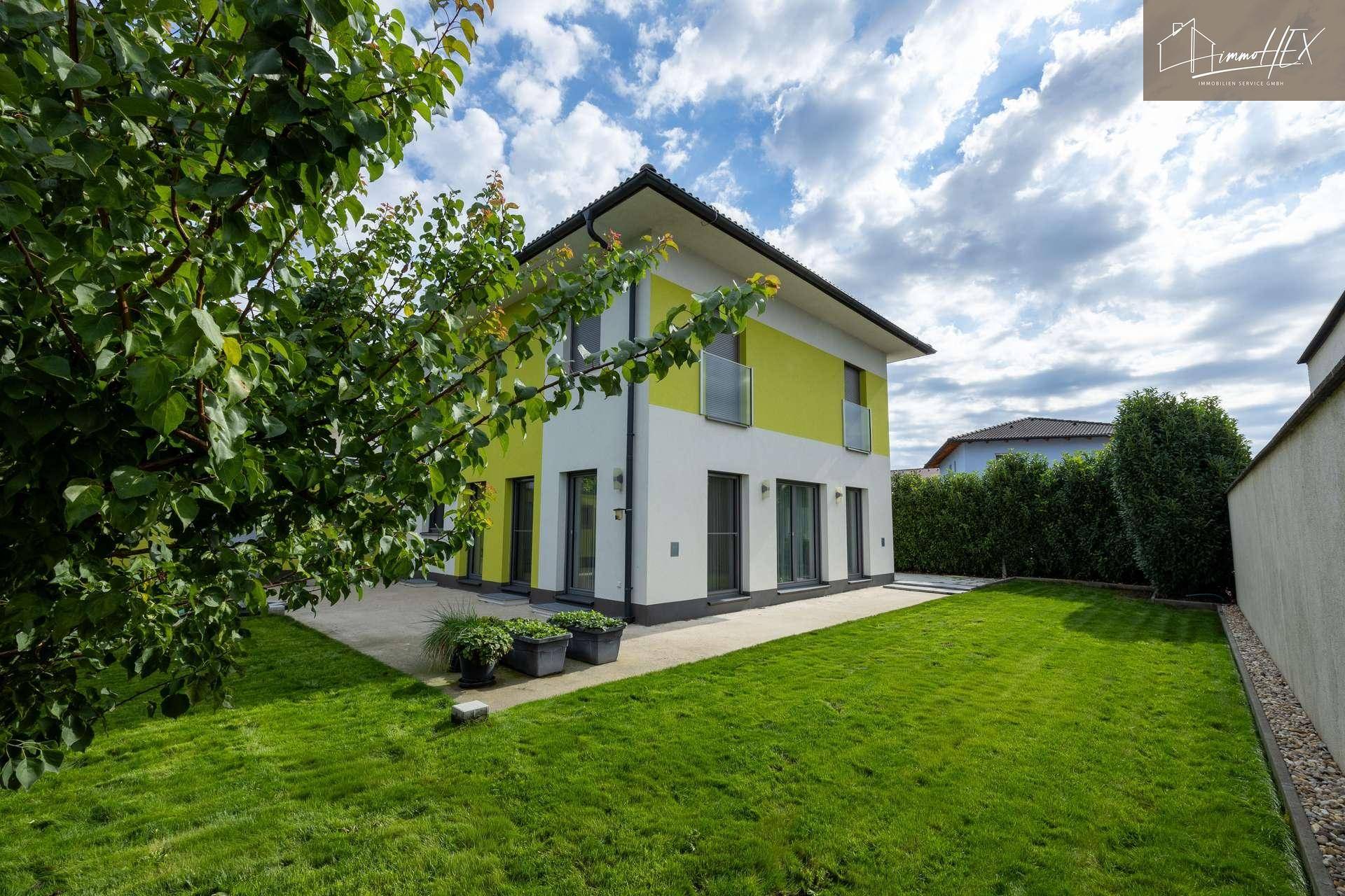 Modernes Einfamilienhaus mit gelb-weißer Fassade und gepflegtem Rasen.