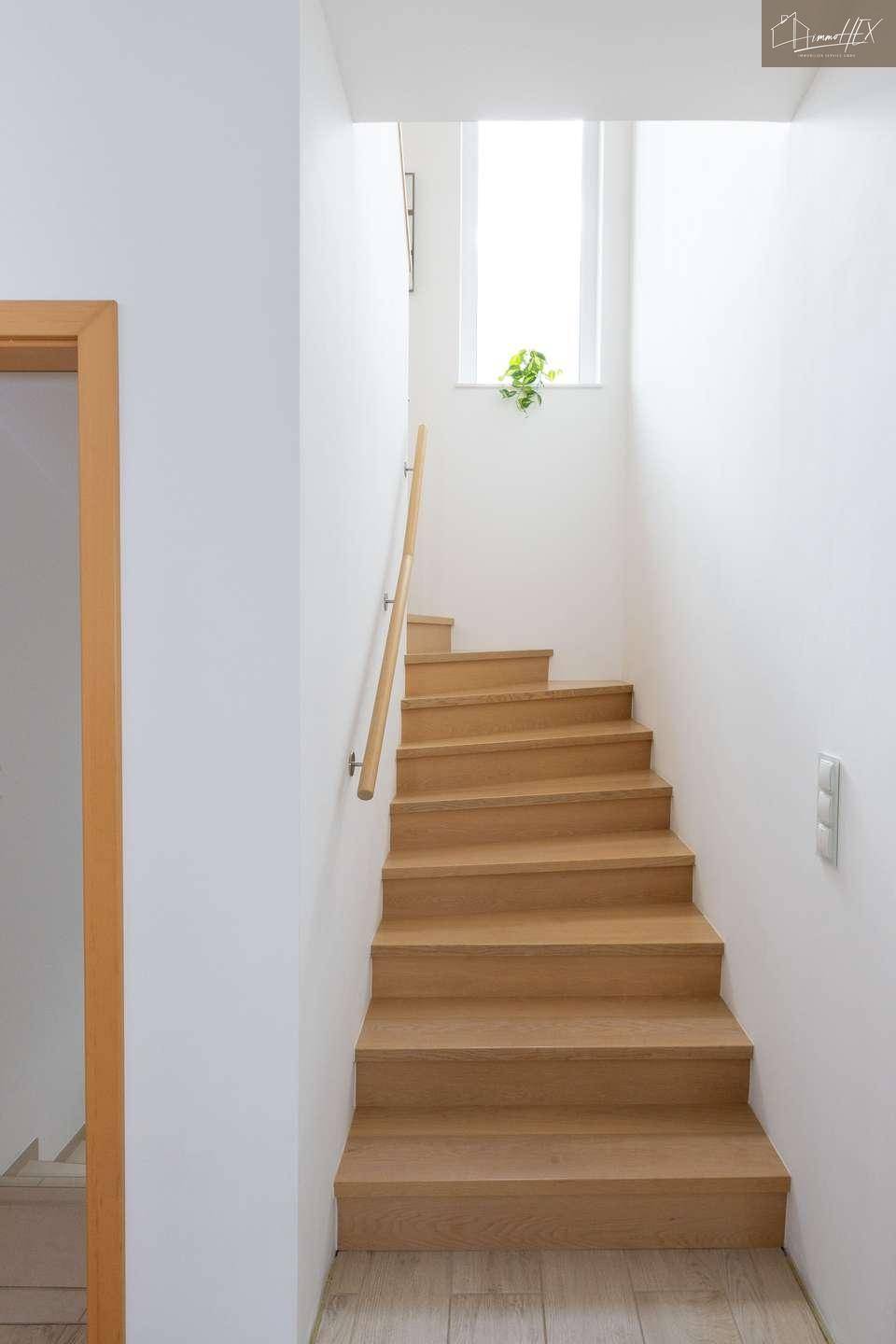 Helles Treppenhaus mit Holzstufen und weiß gestrichenen Wänden, das in die obere Etage führt.