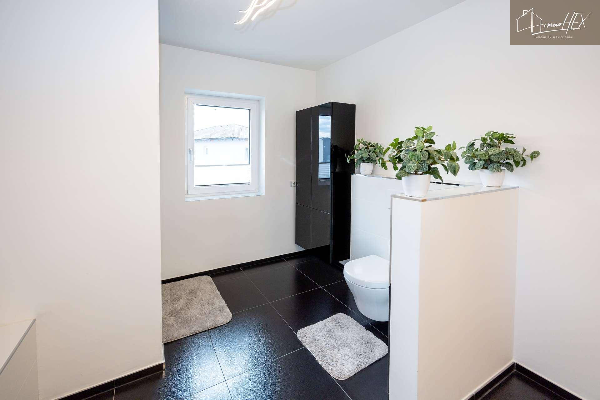 Modernes Badezimmer mit Toilette, Fenster und dunklen Bodenfliesen.
