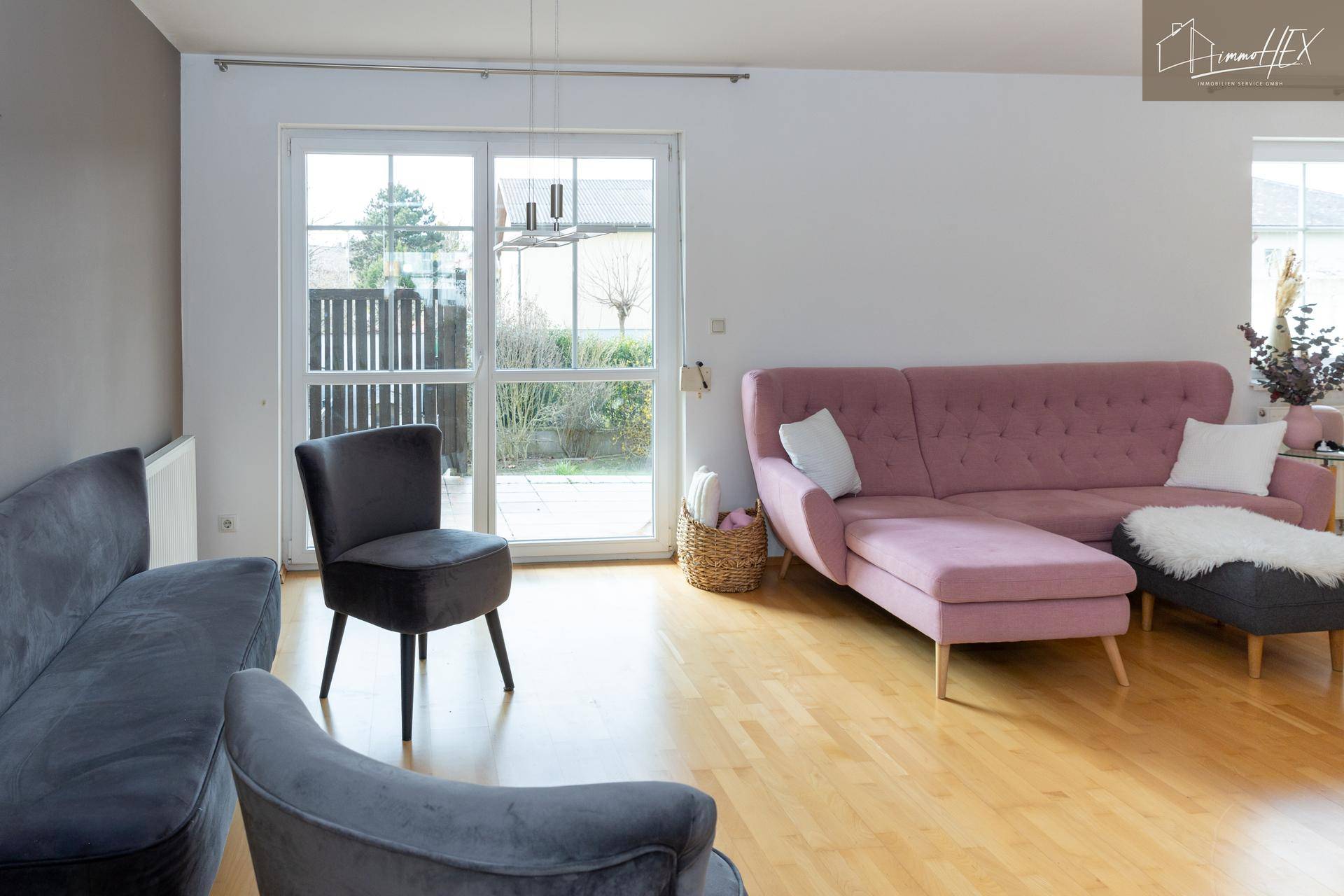 Geräumiges Wohnzimmer mit Holzboden, grauen Sofas und großen Fenstern zum Garten.