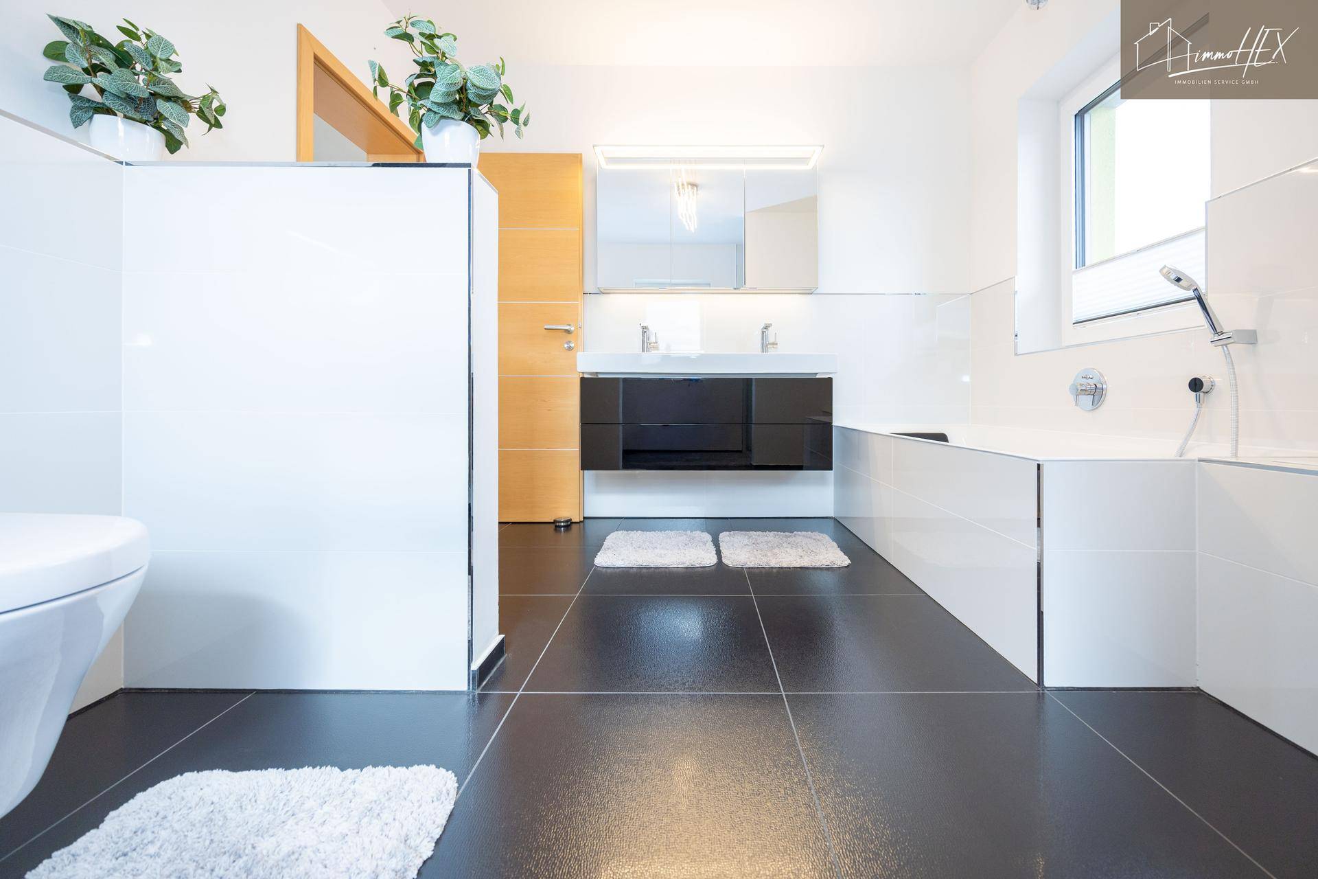 Modernes Badezimmer mit Toilette, Waschbecken und dunklen Bodenfliesen.