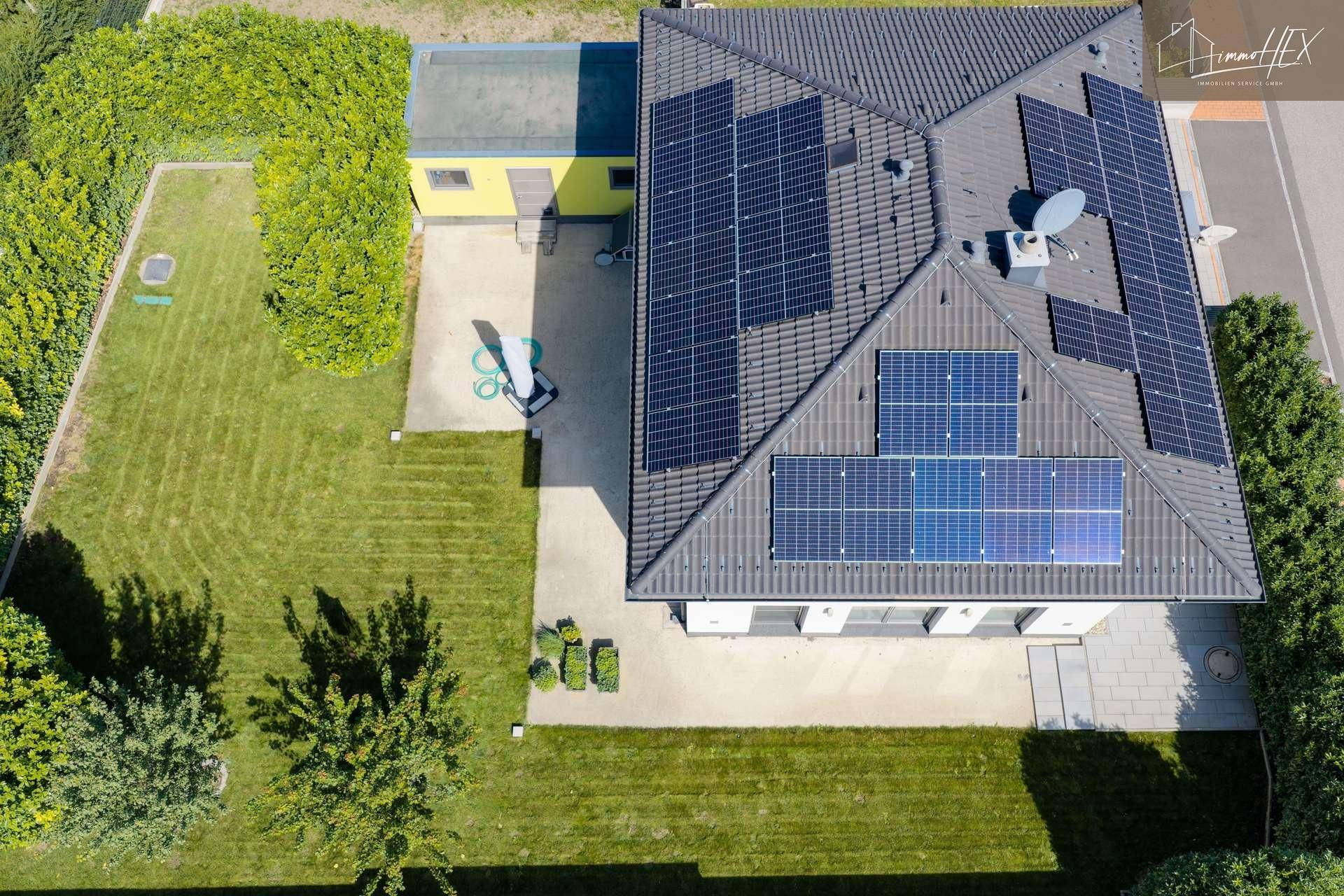 Luftaufnahme eines Hauses mit Photovoltaikanlage auf dem Dach und großem Garten.