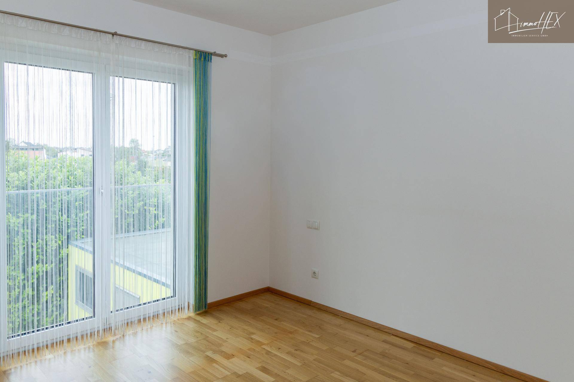 Geräumiges Schlafzimmer mit Holzboden und bodentiefen Fenstern zum Balkon.