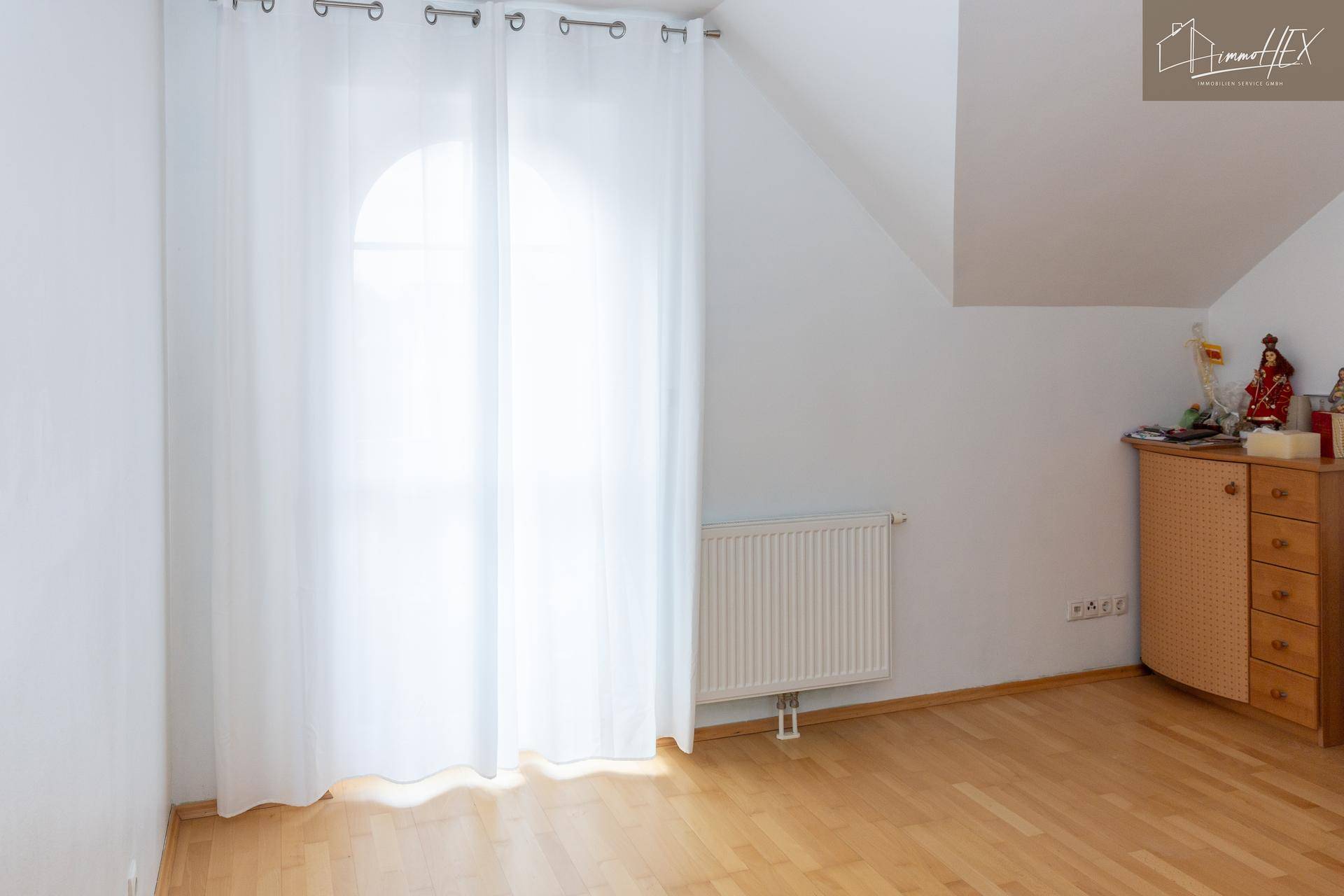 Helles Zimmer im Dachgeschoss mit Holzboden, Fenster und Heizkörper.