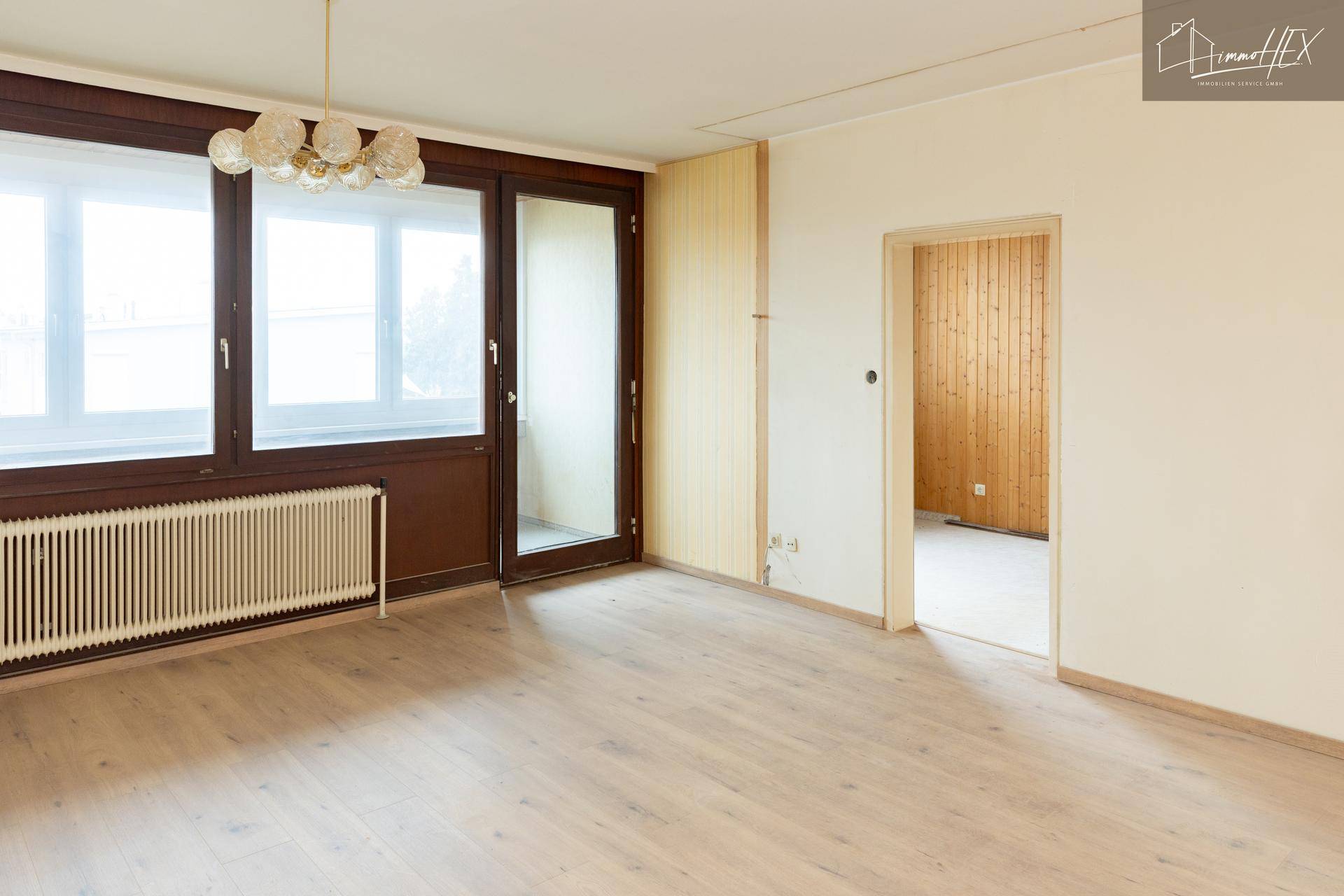 Leeres Wohnzimmer mit Zugang zu einem weiteren Raum und Blick auf den Balkon.