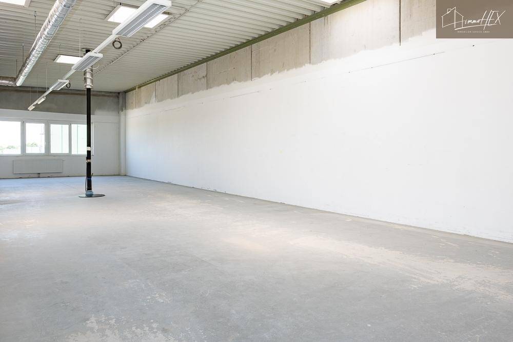 Geräumiger, unmöblierter Bürobereich mit großen Fenstern und einem robusten Betonboden.
