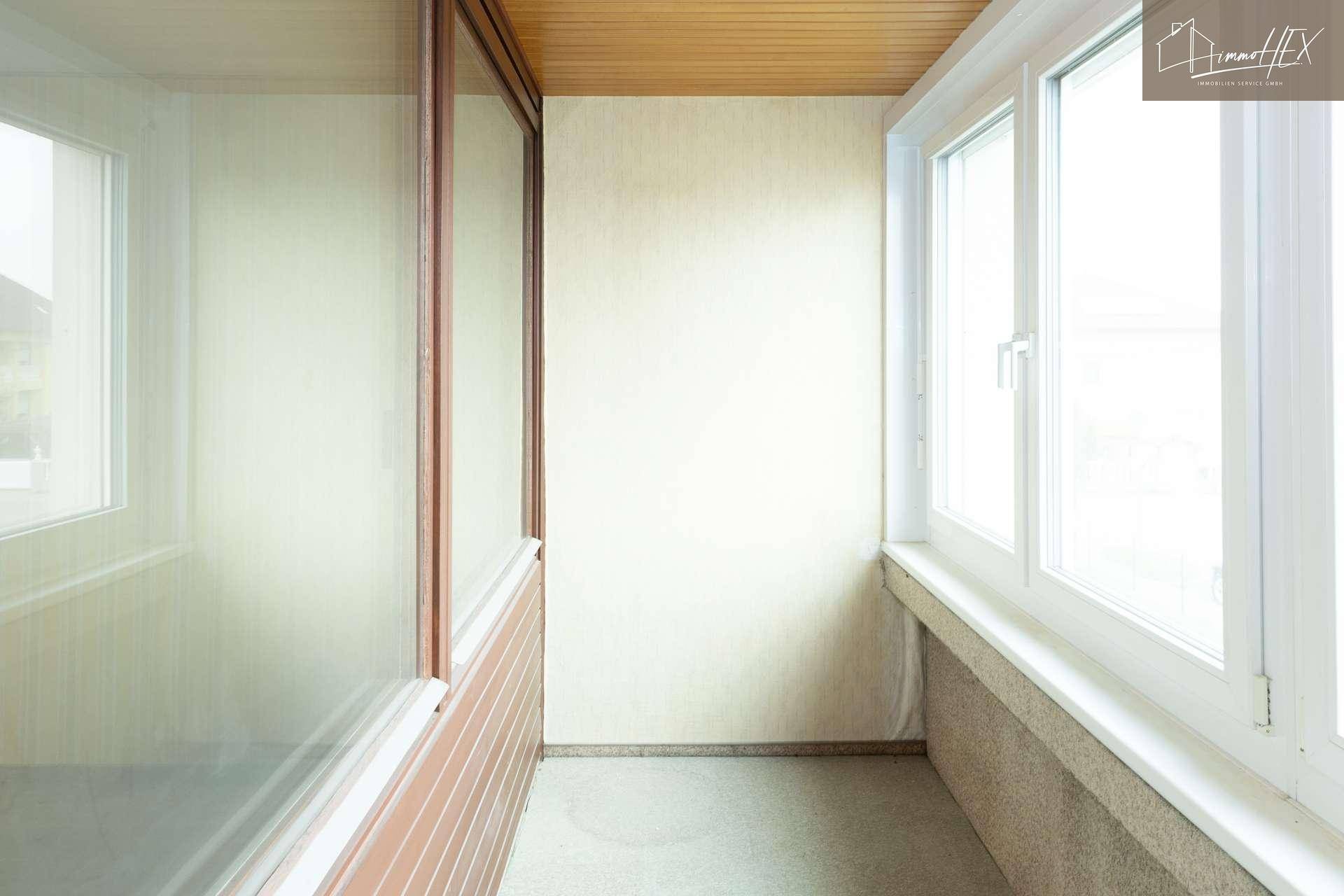 Enge Loggia mit Holzdecke und großen Fenstern, die viel Licht hereinlassen.