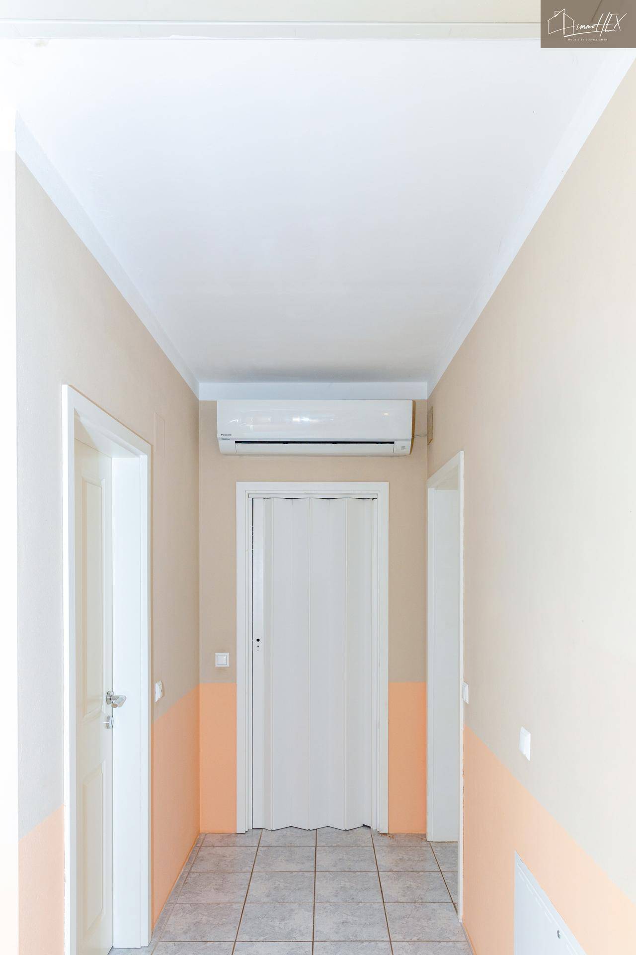 Heller Flur mit Fliesenboden und Klimaanlage, der zu weiteren Räumen führt.