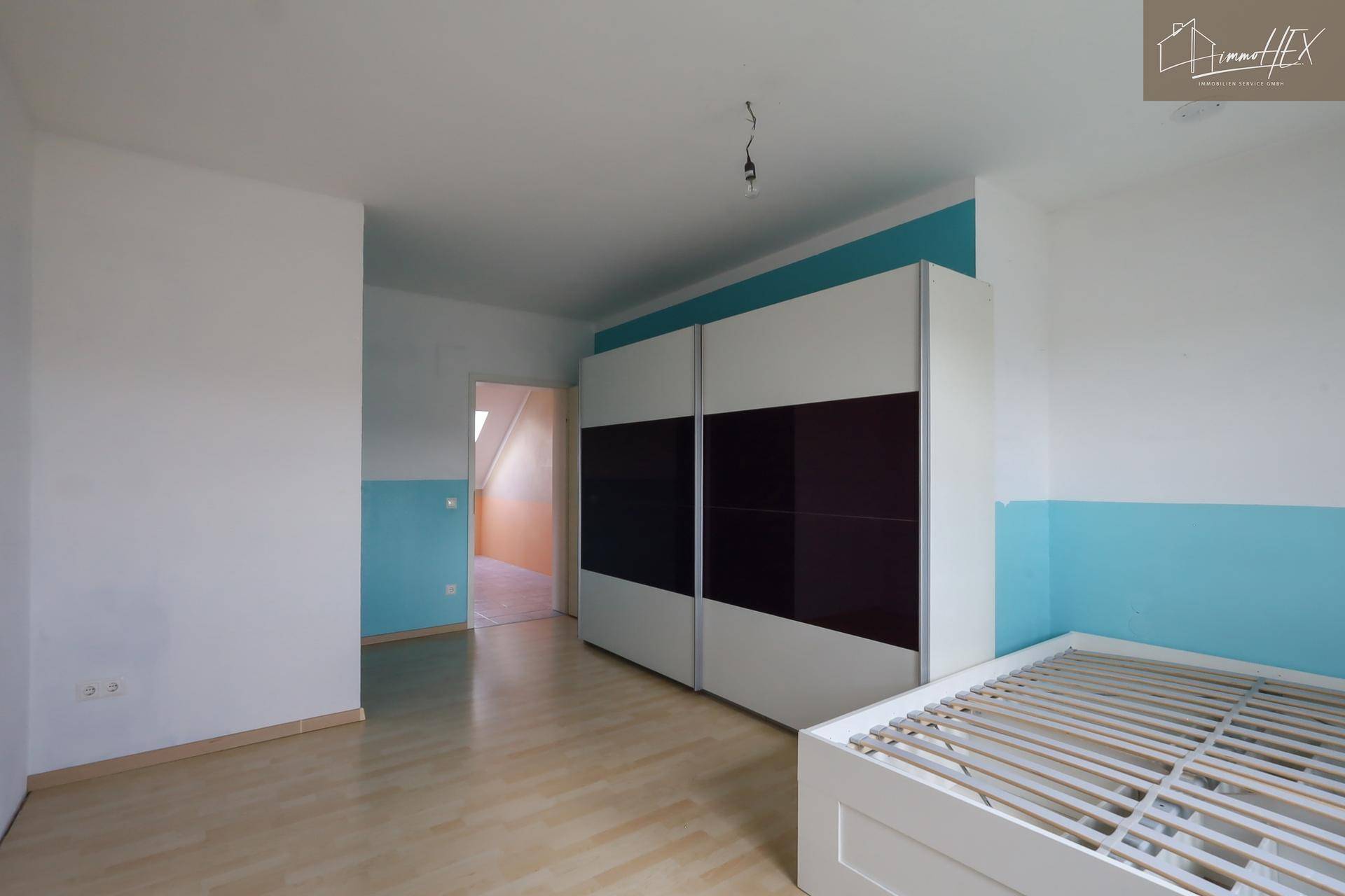 Schlafzimmer mit hellem Laminatboden, farbigen Wänden und einem großen Kleiderschrank.
