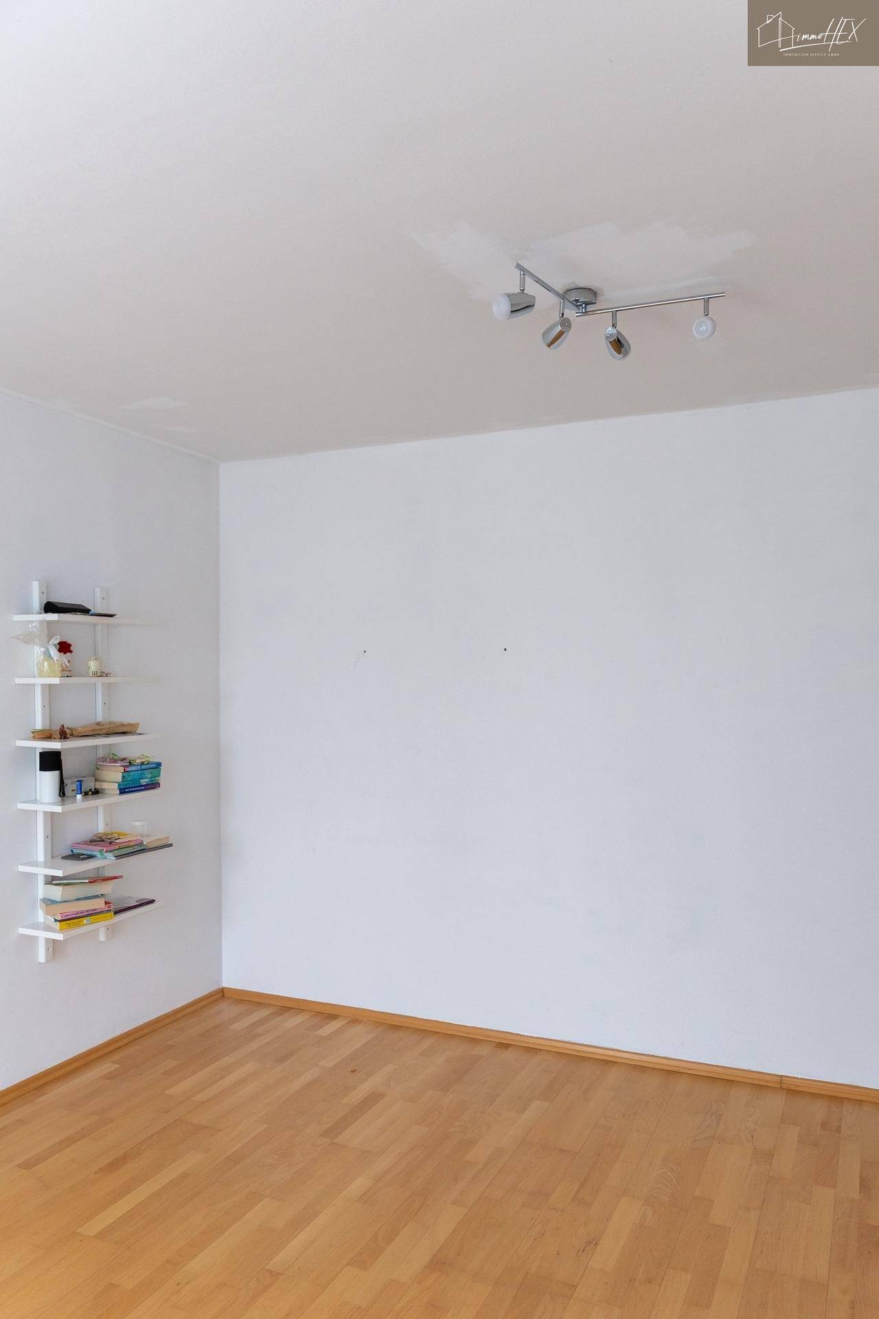 Leeres Zimmer mit Holzboden, weißen Wänden und schwebenden Regalen.