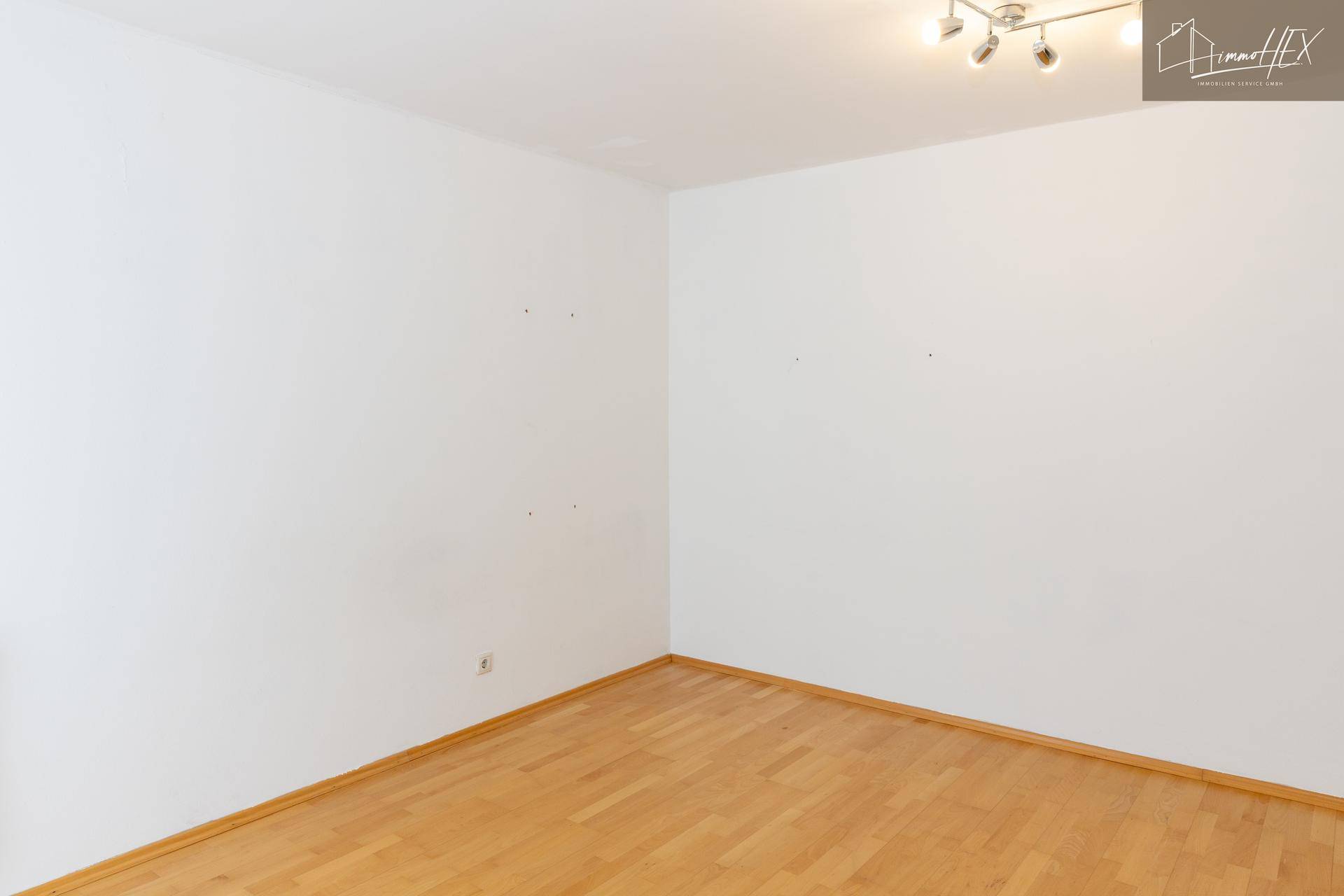 Leeres Zimmer mit Holzboden und weiß gestrichenen Wänden, bereit zur individuellen Gestaltung.