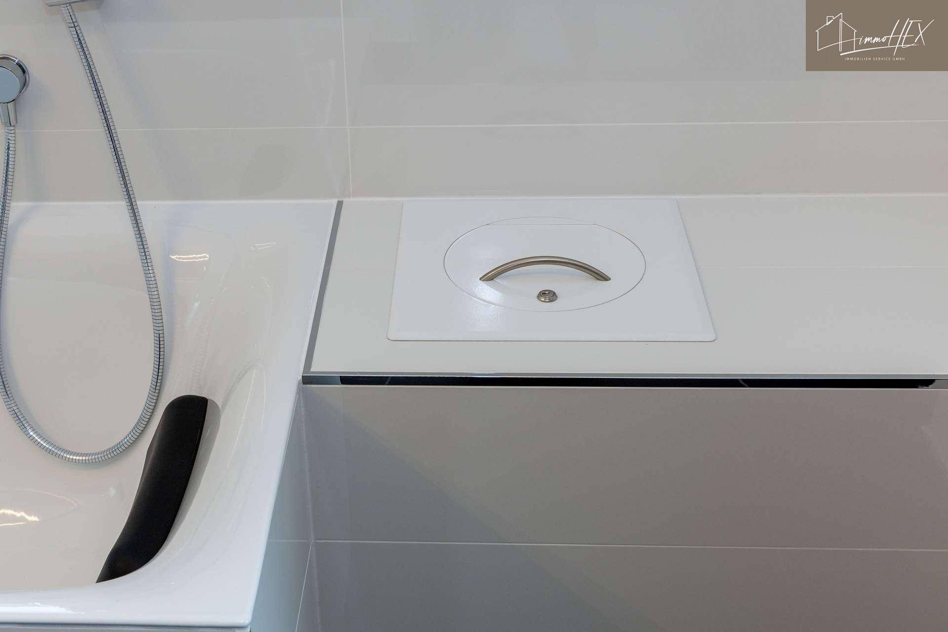 Detailansicht einer Badewanne mit Duschkopf und integriertem Wäscheabwurf.