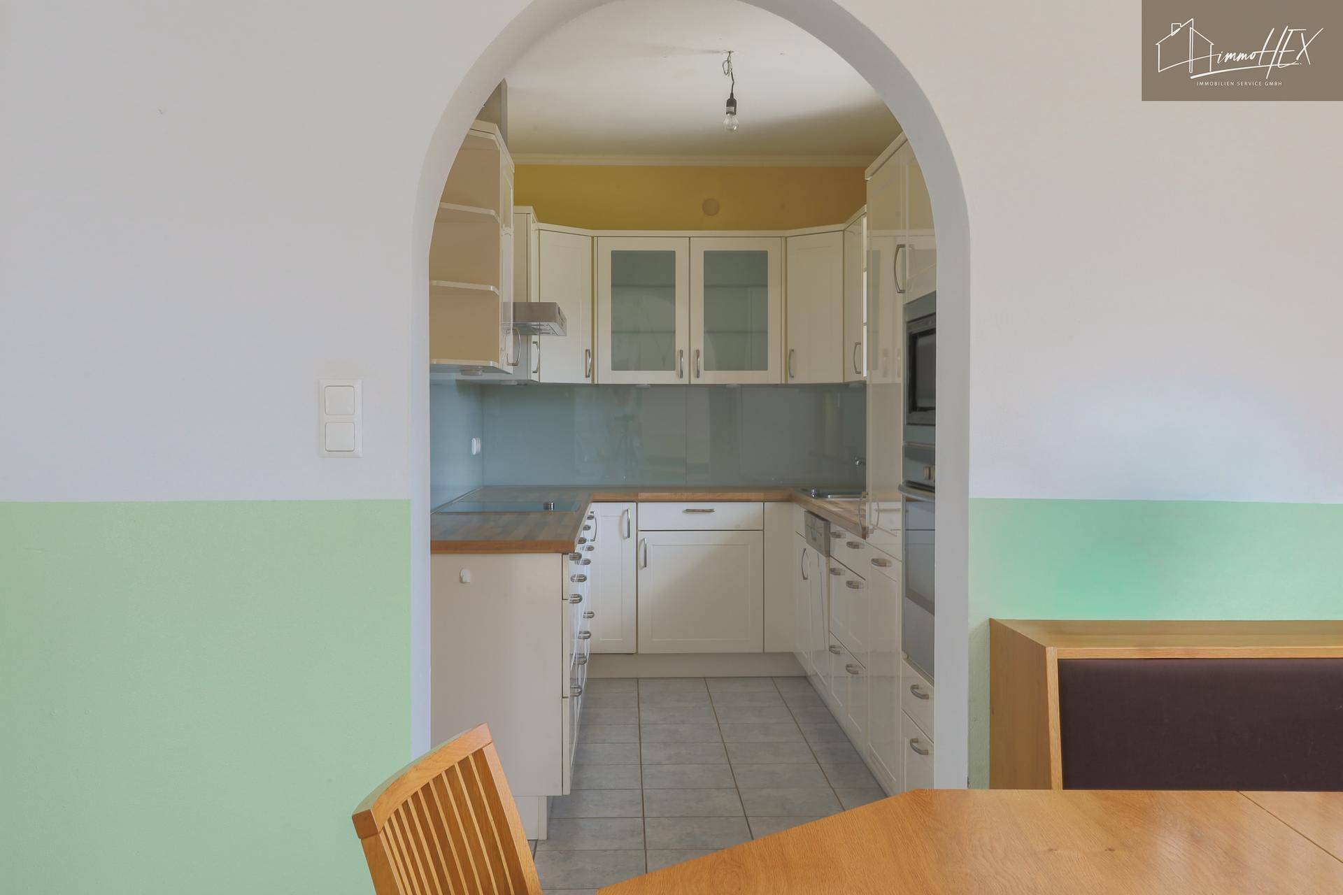 Blick durch einen Bogen in eine Küche mit weißen Schränken und hellblauer Rückwand.