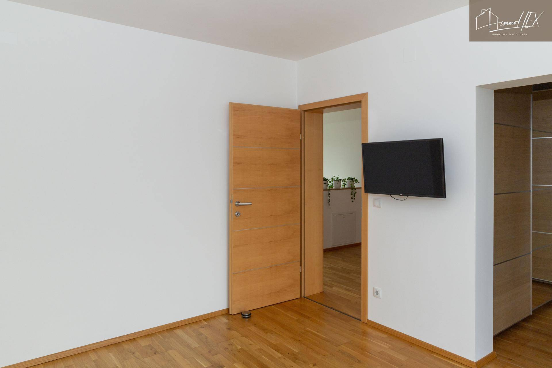 Helles Zimmer mit Holzboden, Holztür und einem an der Wand montierten Fernseher.