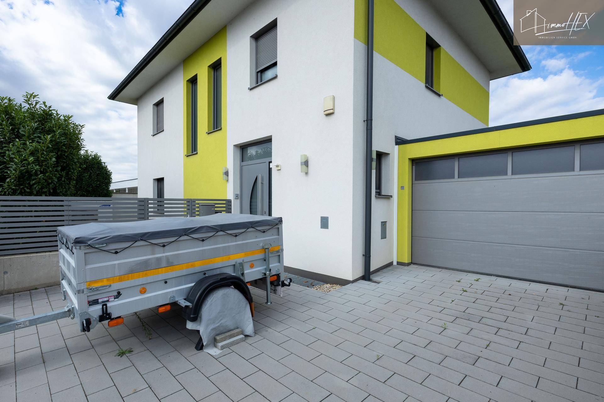 Modernes Haus mit gelben Akzenten, gepflasterter Einfahrt und einer Garage mit Rolltor.