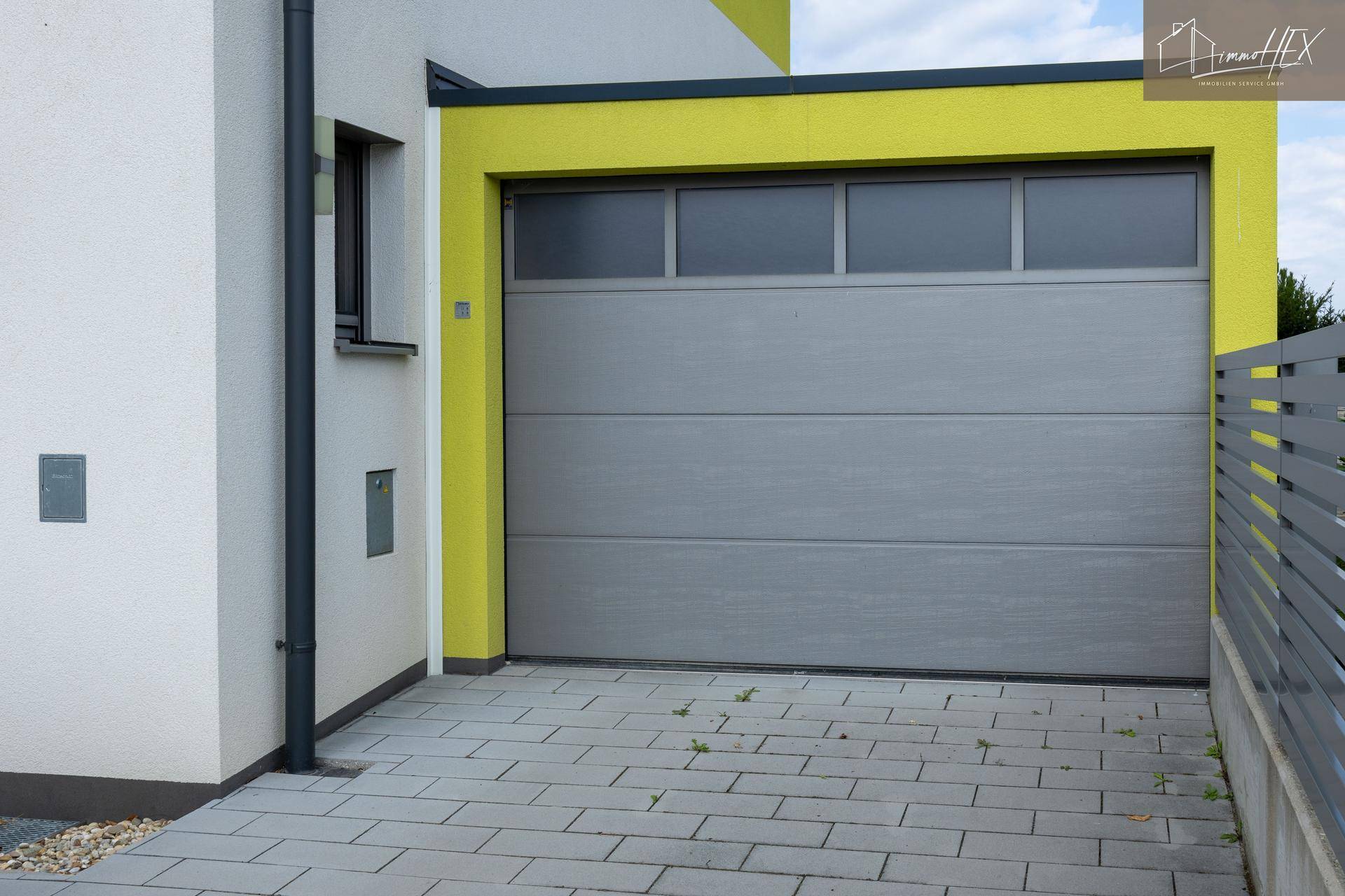 Moderne Garage mit Sektionaltor und gepflasterter Zufahrt, integriert in das Hausdesign.