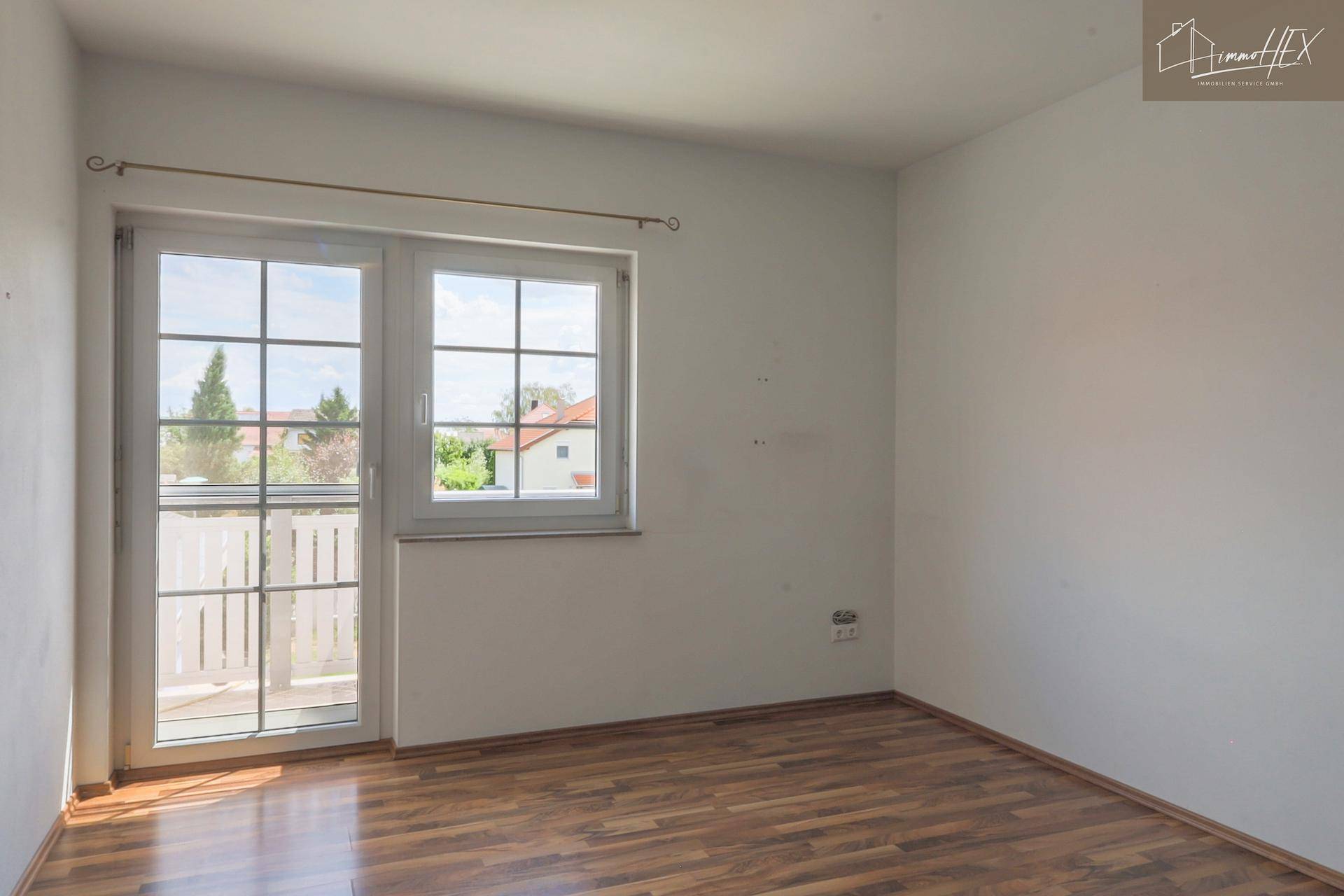 Helles Schlafzimmer mit Laminatboden und großem Fenster, das viel Tageslicht hereinlässt.
