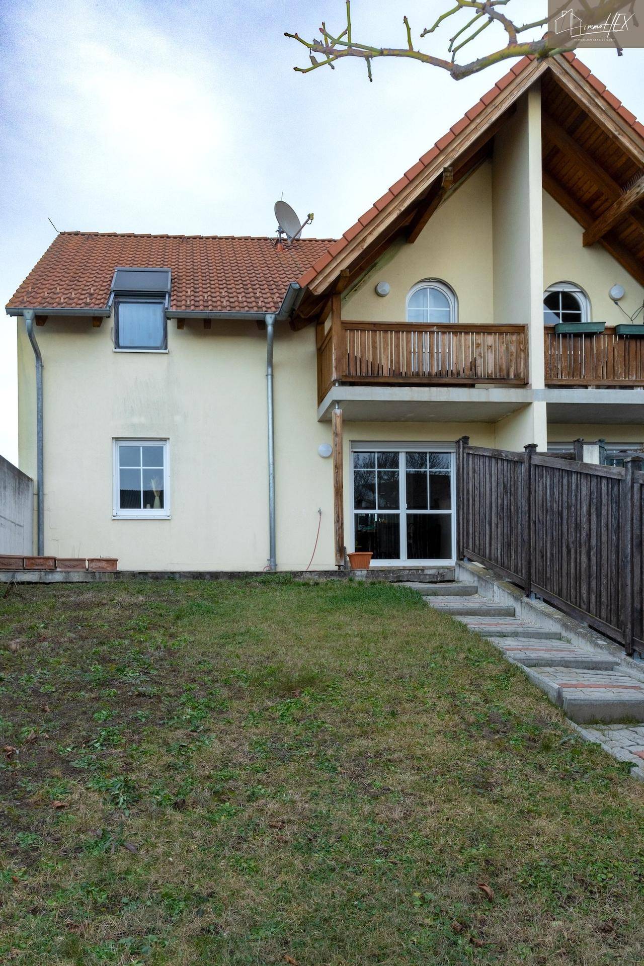 Ansicht des Hauses mit gelber Fassade, rotem Ziegeldach und Balkon.