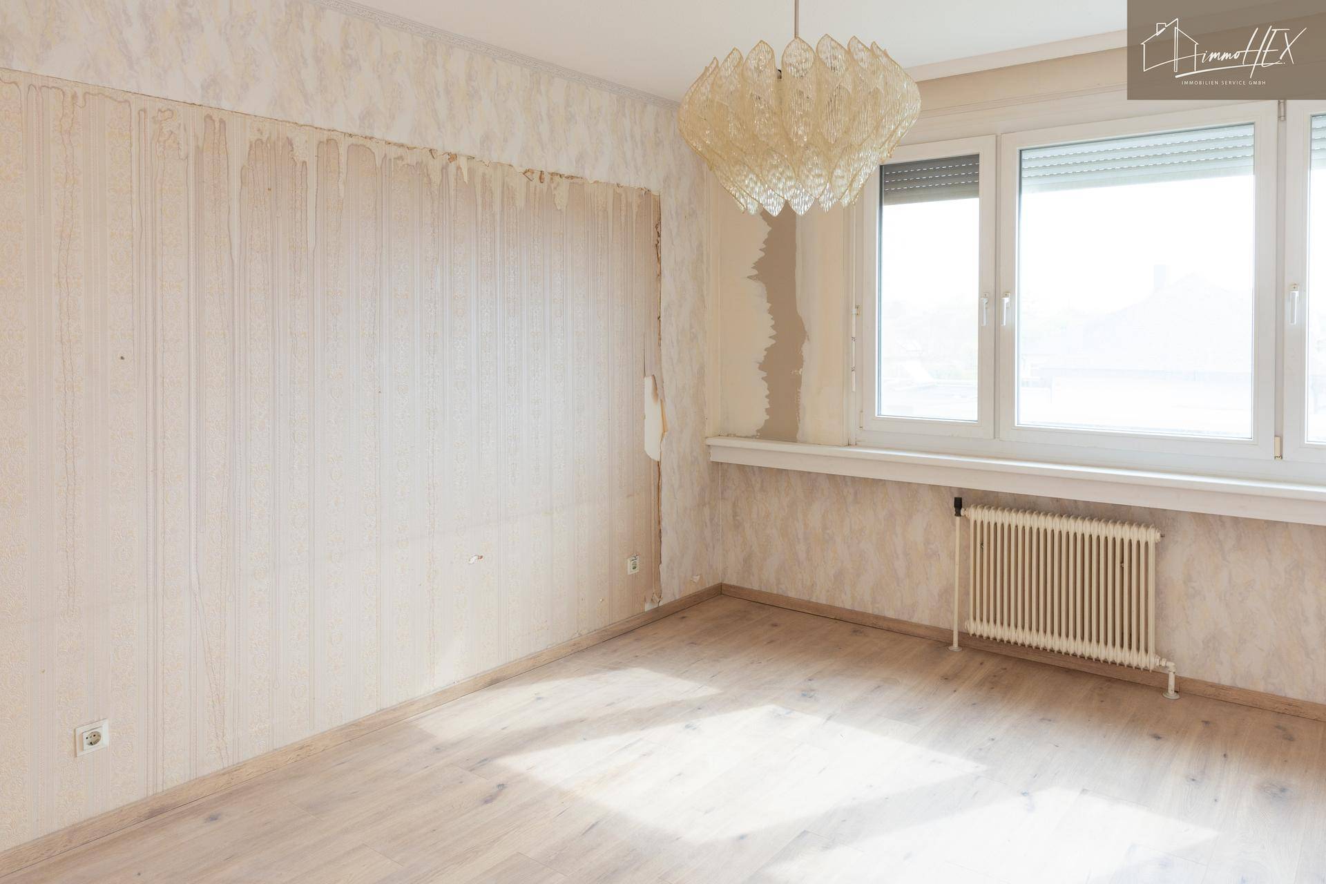 Leeres Schlafzimmer mit teilweise entfernter Tapete und großem Fenster, bereit zur Renovierung.