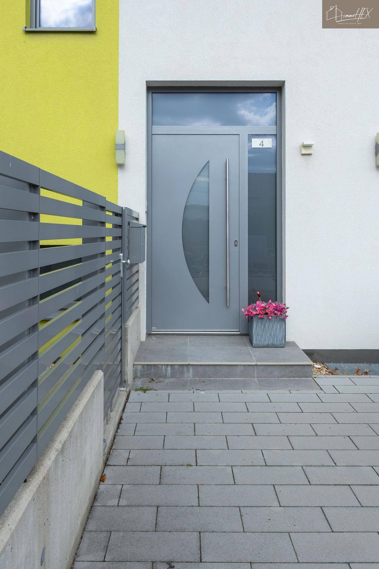 Moderner Hauseingang mit grauer Tür, Seitenteil und einem dekorativen Blumenkübel.