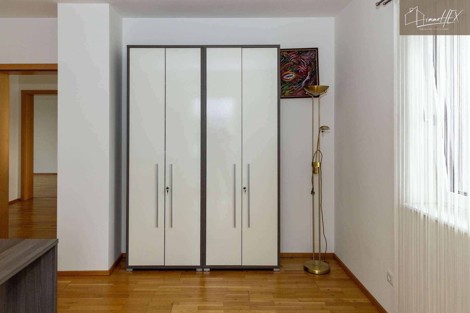 Weißer Kleiderschrank mit Kunstwerk und Stehlampe in einem hellen Raum.