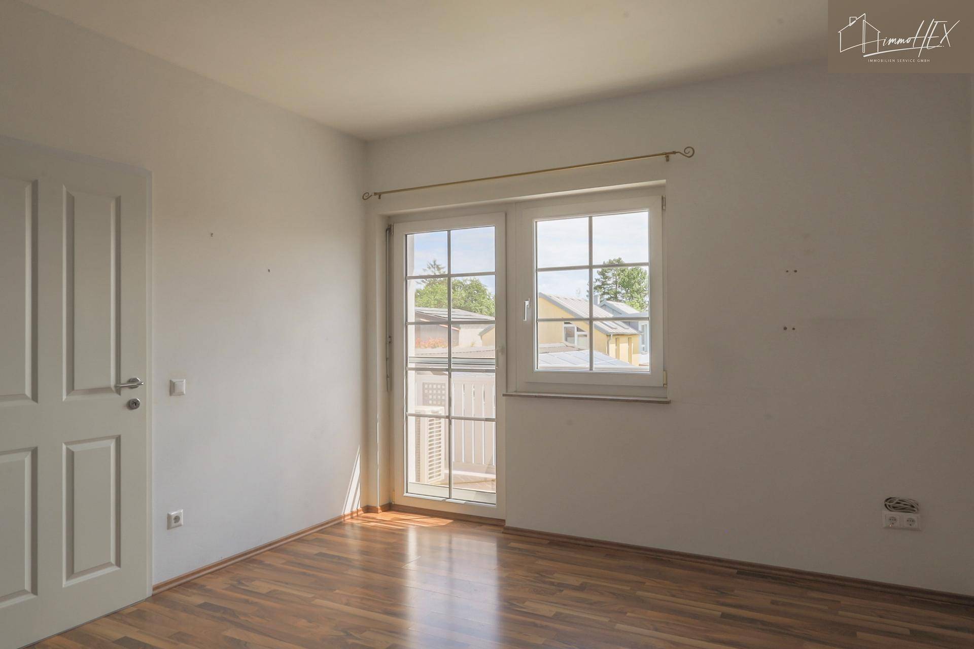 Schlafzimmer mit Laminatboden, hellen Wänden und Zugang zu einem kleinen Balkon oder einer französischen Brüstung.