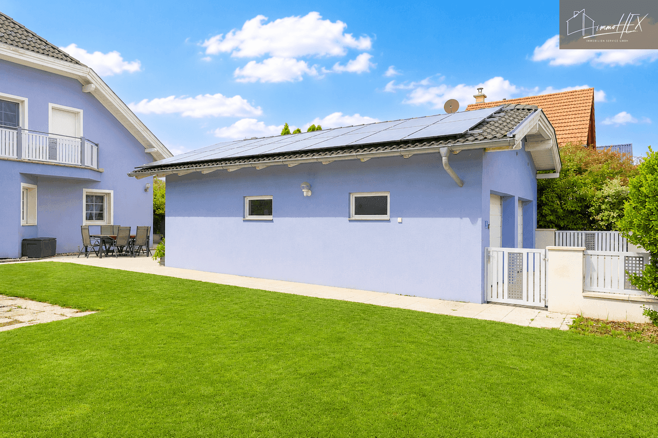 Rückansicht des Hauses mit blauer Fassade, Garten und Photovoltaikanlage auf dem Garagendach.