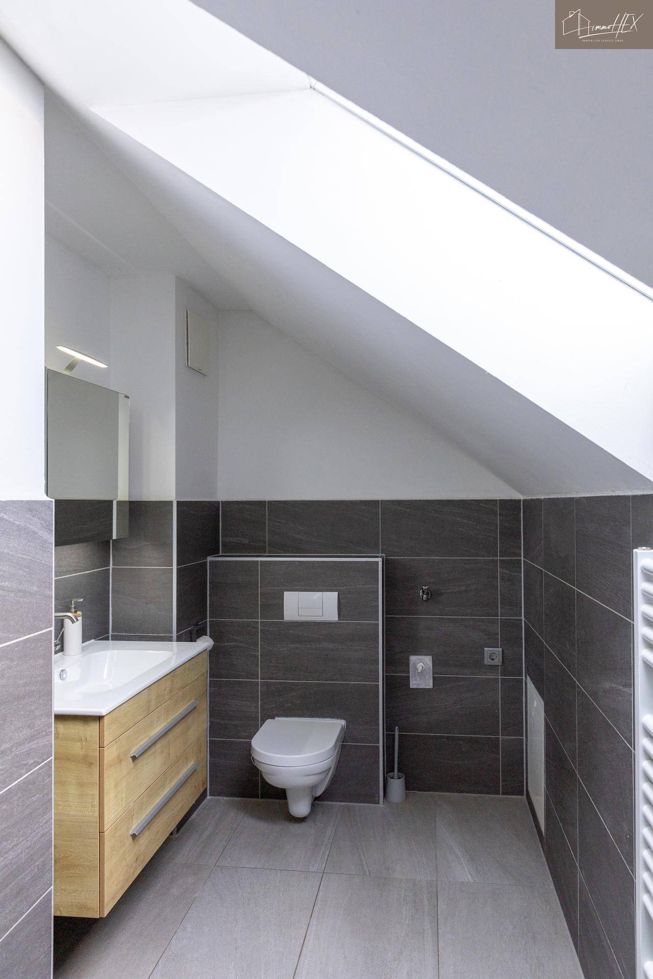 Modernes Badezimmer mit wandhängendem WC, Waschbecken und grauen Fliesen.