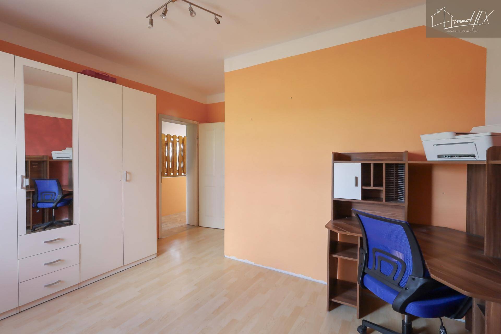 Arbeitszimmer mit hellem Laminatboden, orangefarbenen Wänden und einem Schreibtischbereich.