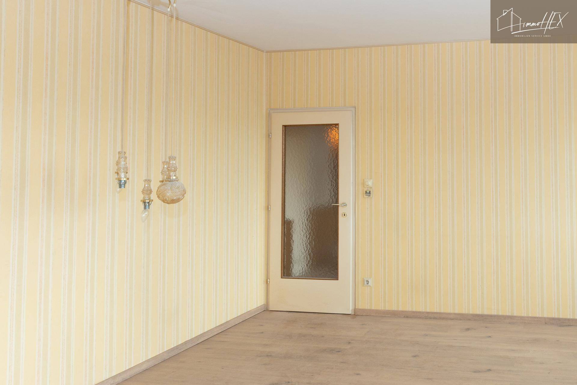 Leerer Raum mit gestreifter Tapete und einer Tür mit Milchglas, die zu einem anderen Bereich führt.