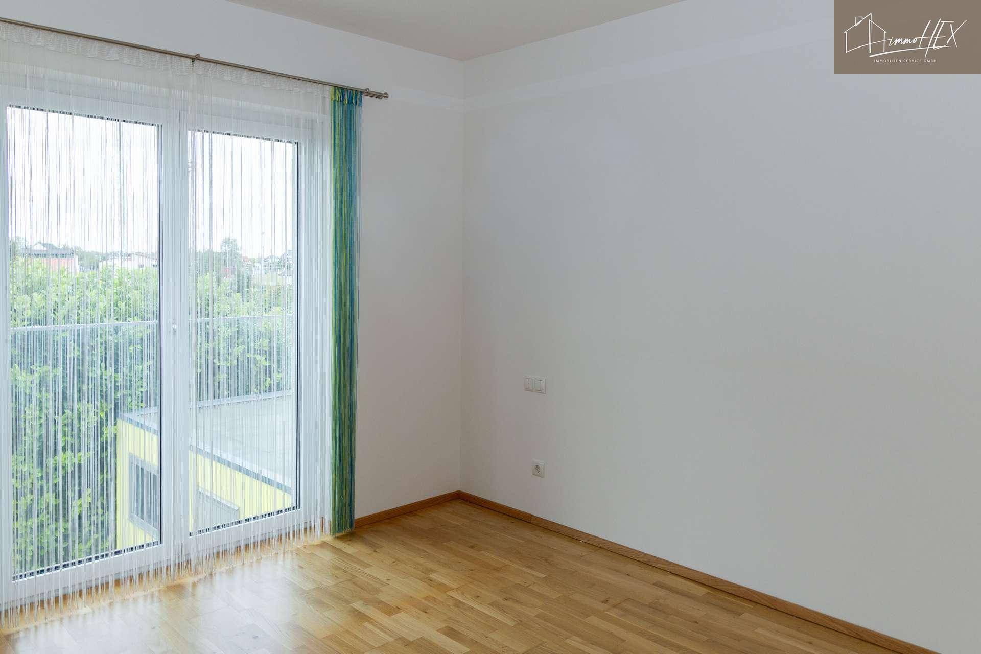 Lichtdurchflutetes Zimmer mit Parkettboden und weiten Fenstern, die einen Blick ins Grüne bieten.