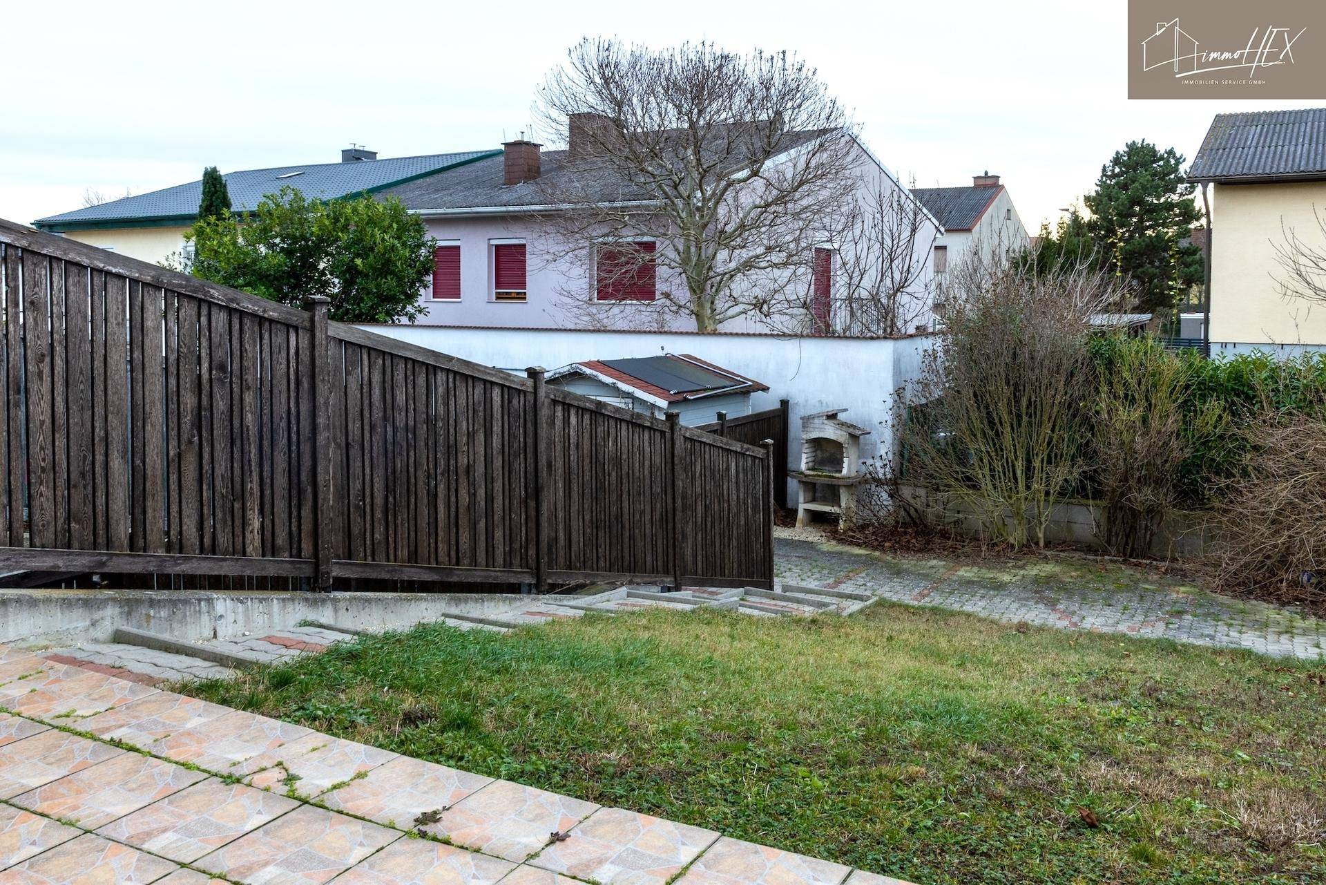Gartenbereich mit Rasenfläche, Holzzaun und gemauertem Grillplatz.