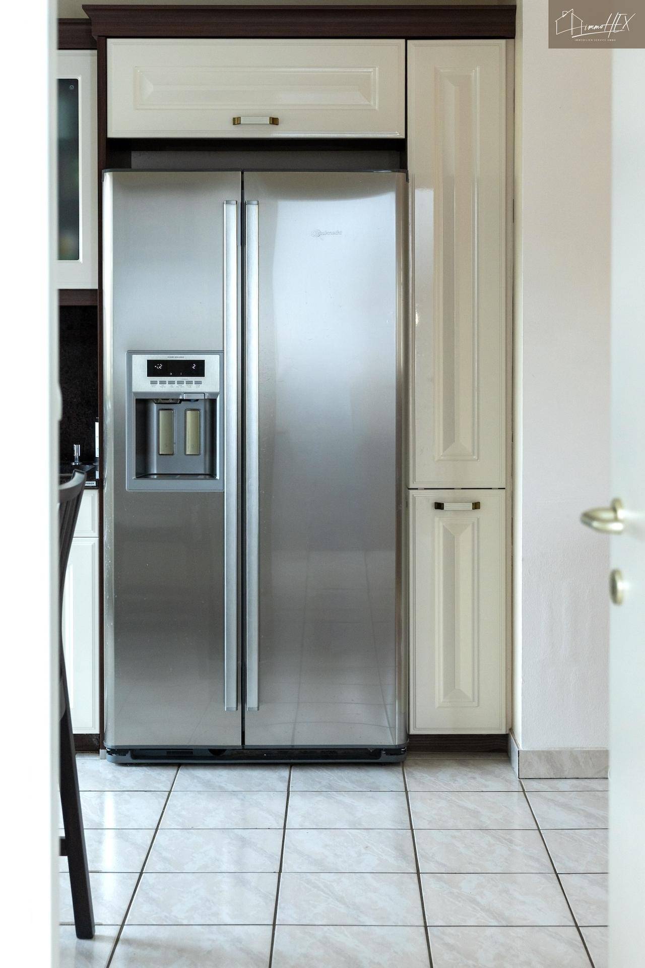 Großer amerikanischer Kühlschrank in der Küche mit weißen Schränken und Fliesenboden.