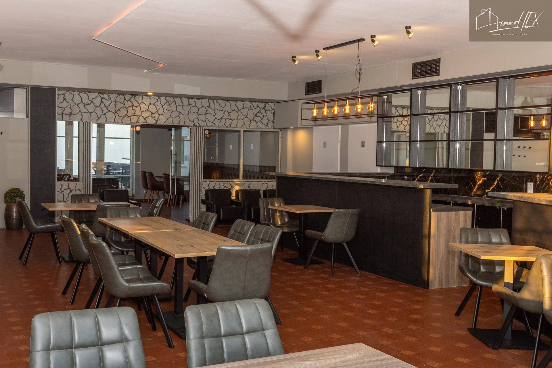 Großer Gastraum mit Terrakottafliesen, bequemen Stühlen und einer modernen Bar.