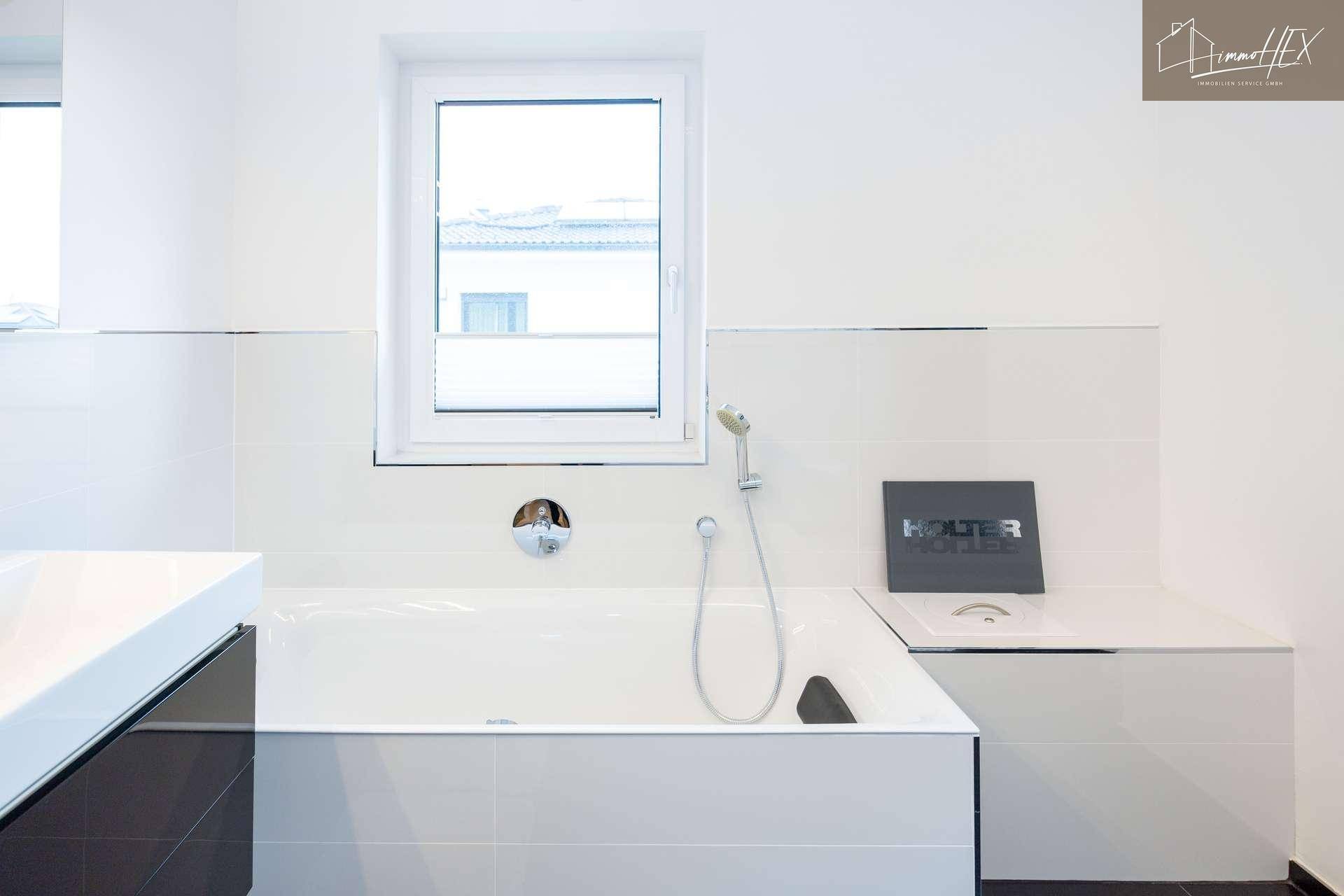 Eingebaute Badewanne unter einem Fenster im hellen Badezimmer, mit moderner Duscharmatur.