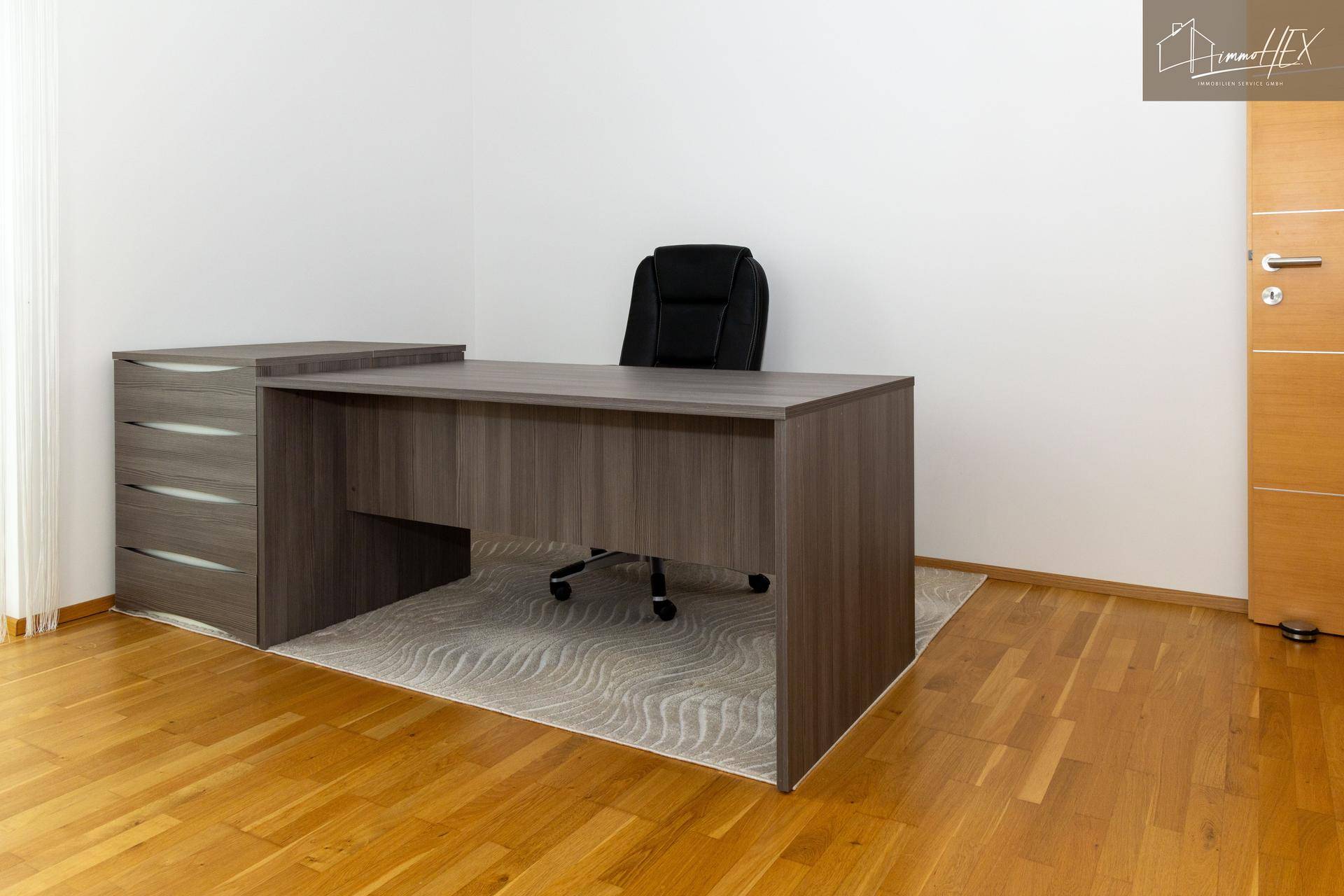 Moderner Schreibtisch mit Bürostuhl auf Teppich und Holzboden in einem hellen Raum.
