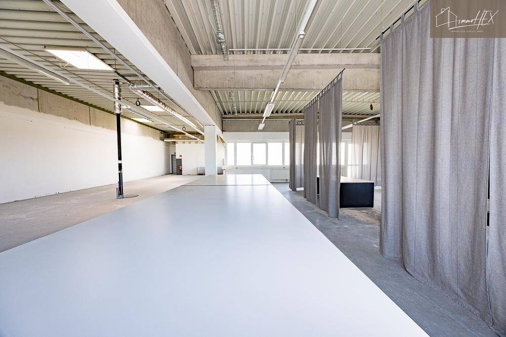 Langer Arbeitstisch im Vordergrund eines offenen Bürobereichs mit industriellem Design.