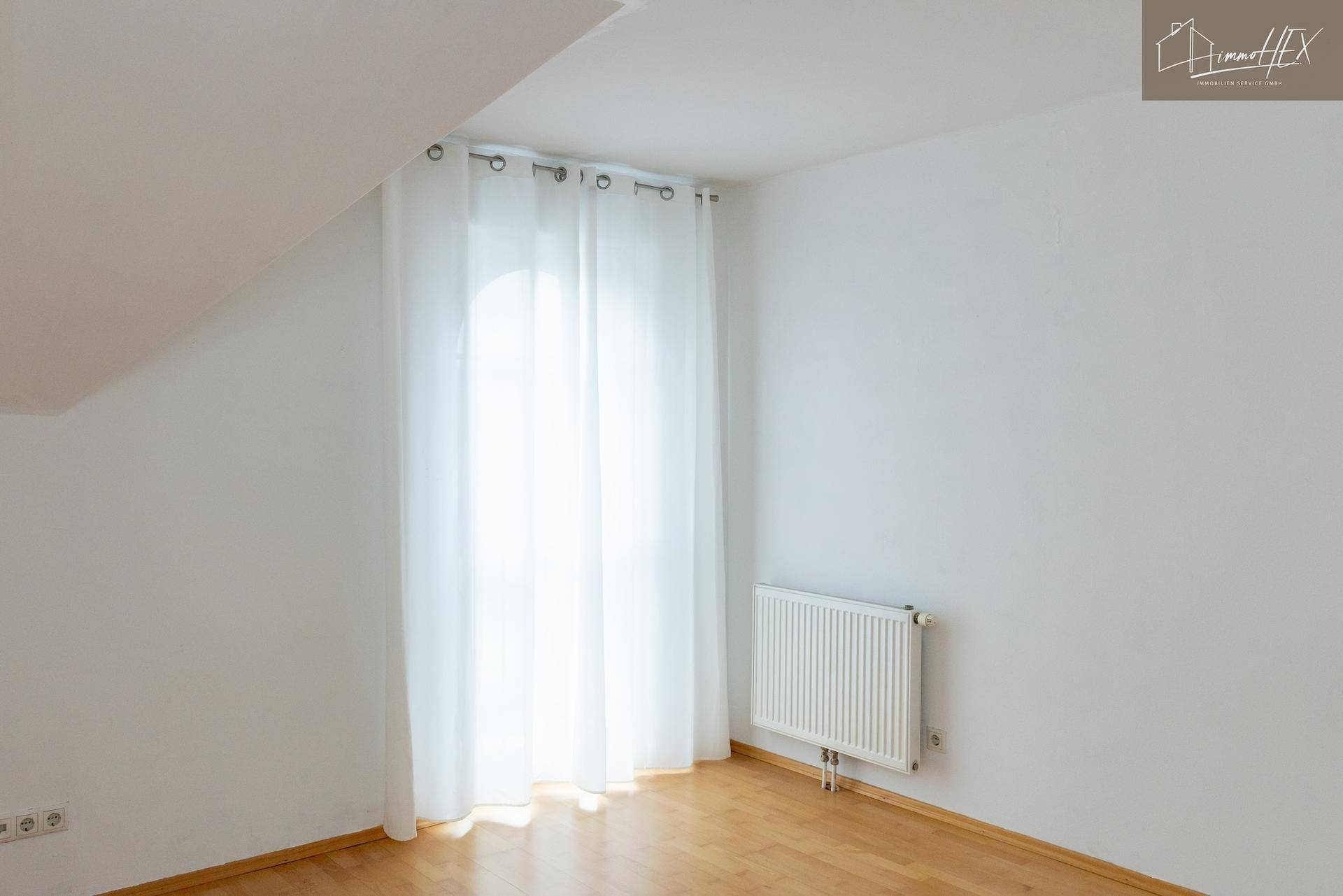 Helles Zimmer im Dachgeschoss mit Holzboden, Fenster und Heizkörper.
