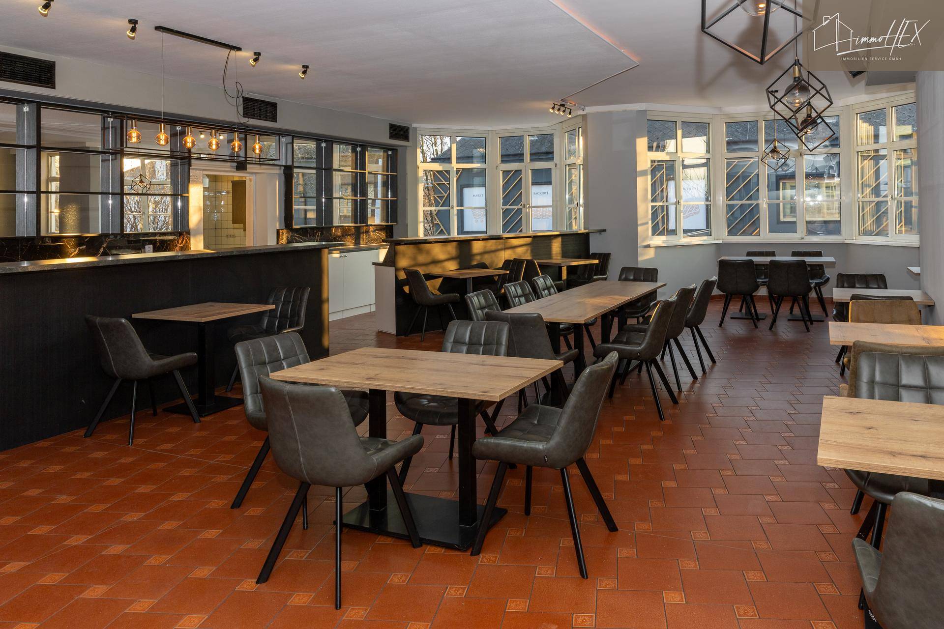 Einladender Gastraum mit viel Tageslicht, bequemen Sitzgelegenheiten und einer eleganten Bar.