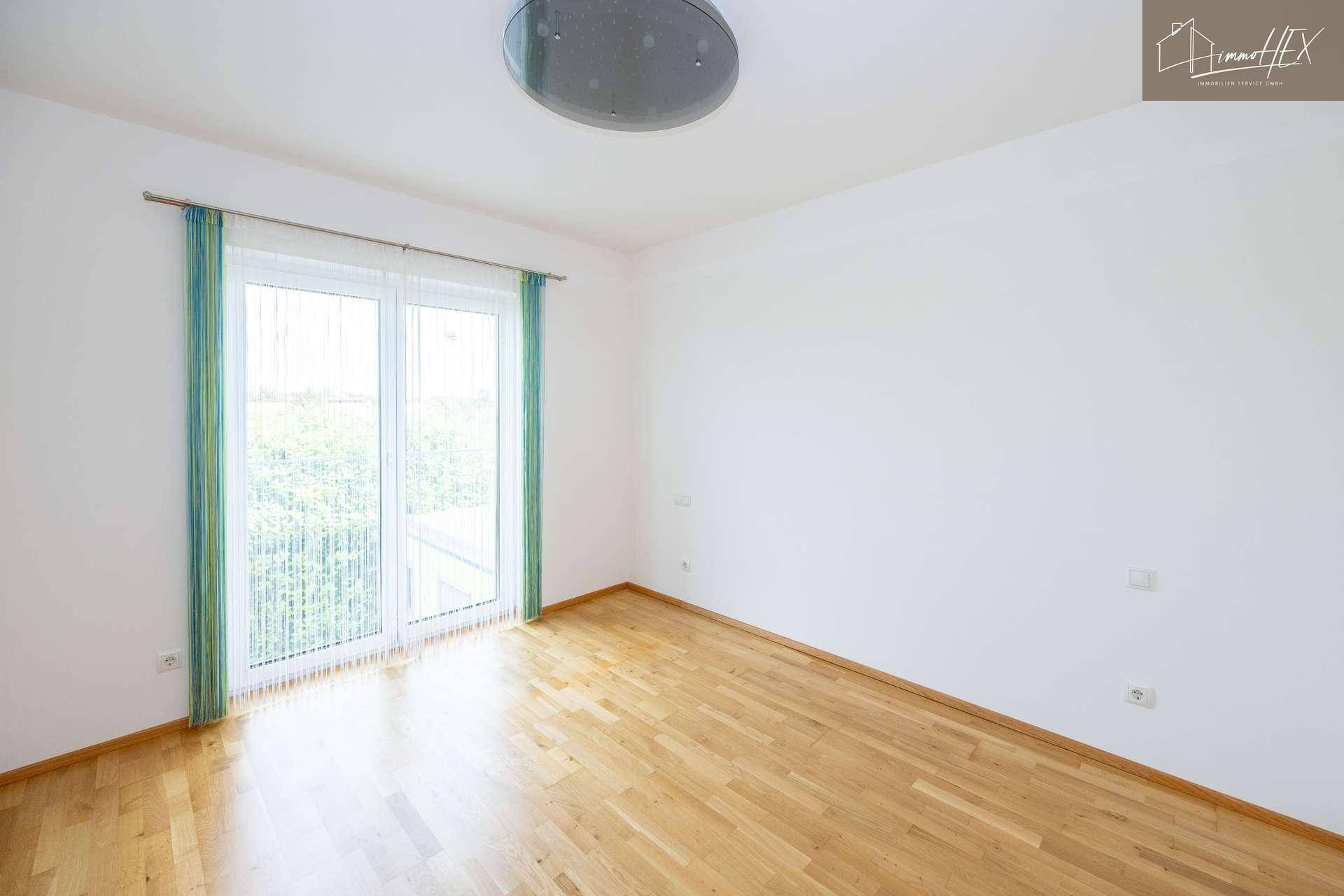 Helles Schlafzimmer mit Holzboden und großem Fenster, das Zugang zum Balkon bietet.