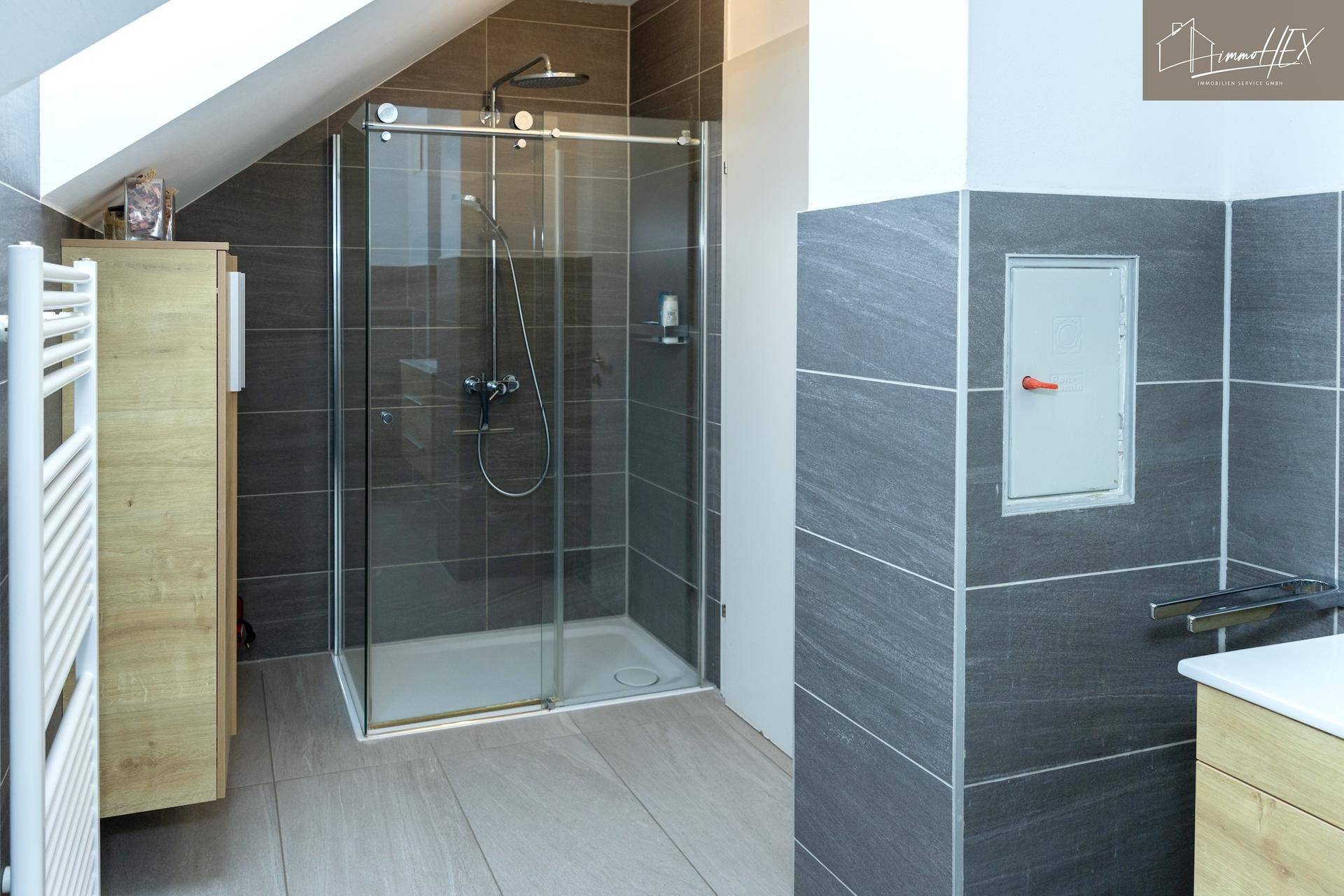 Modernes Badezimmer mit großer Duschkabine und grauen Wandfliesen.