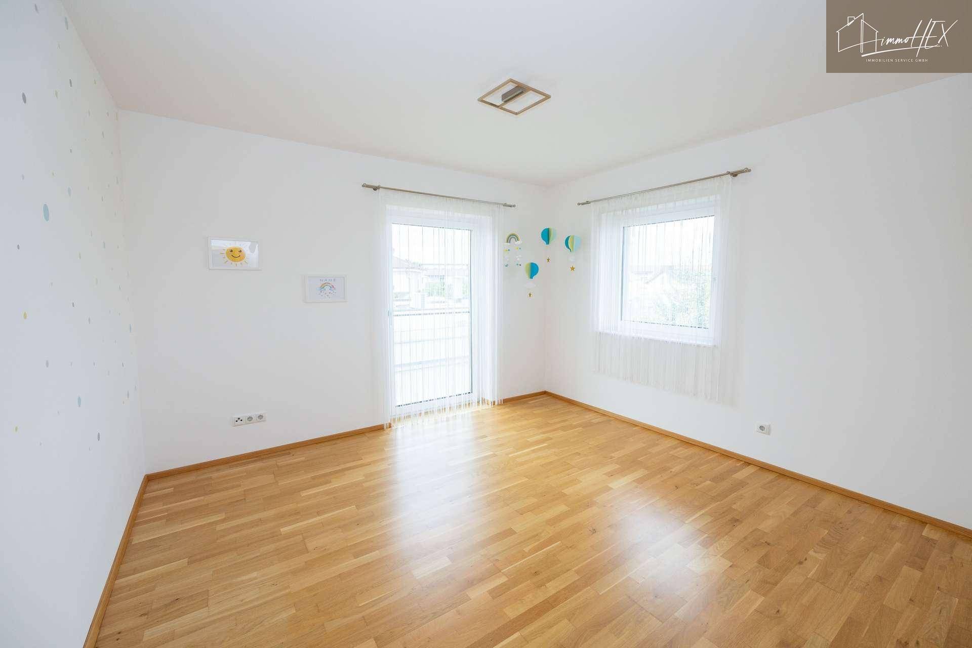 Helles Kinderzimmer mit Holzboden, großen Fenstern und Zugang zu einem Balkon.