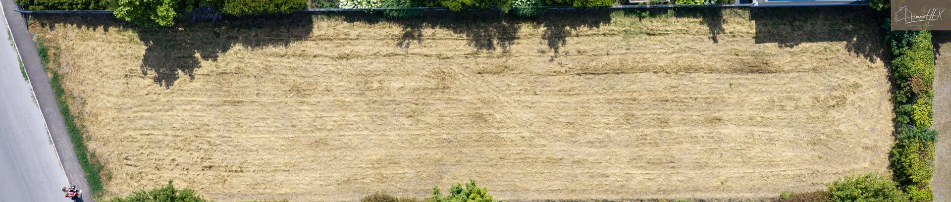 Luftaufnahme eines länglichen Grundstücks mit trockener Grasfläche und angrenzender Straße.